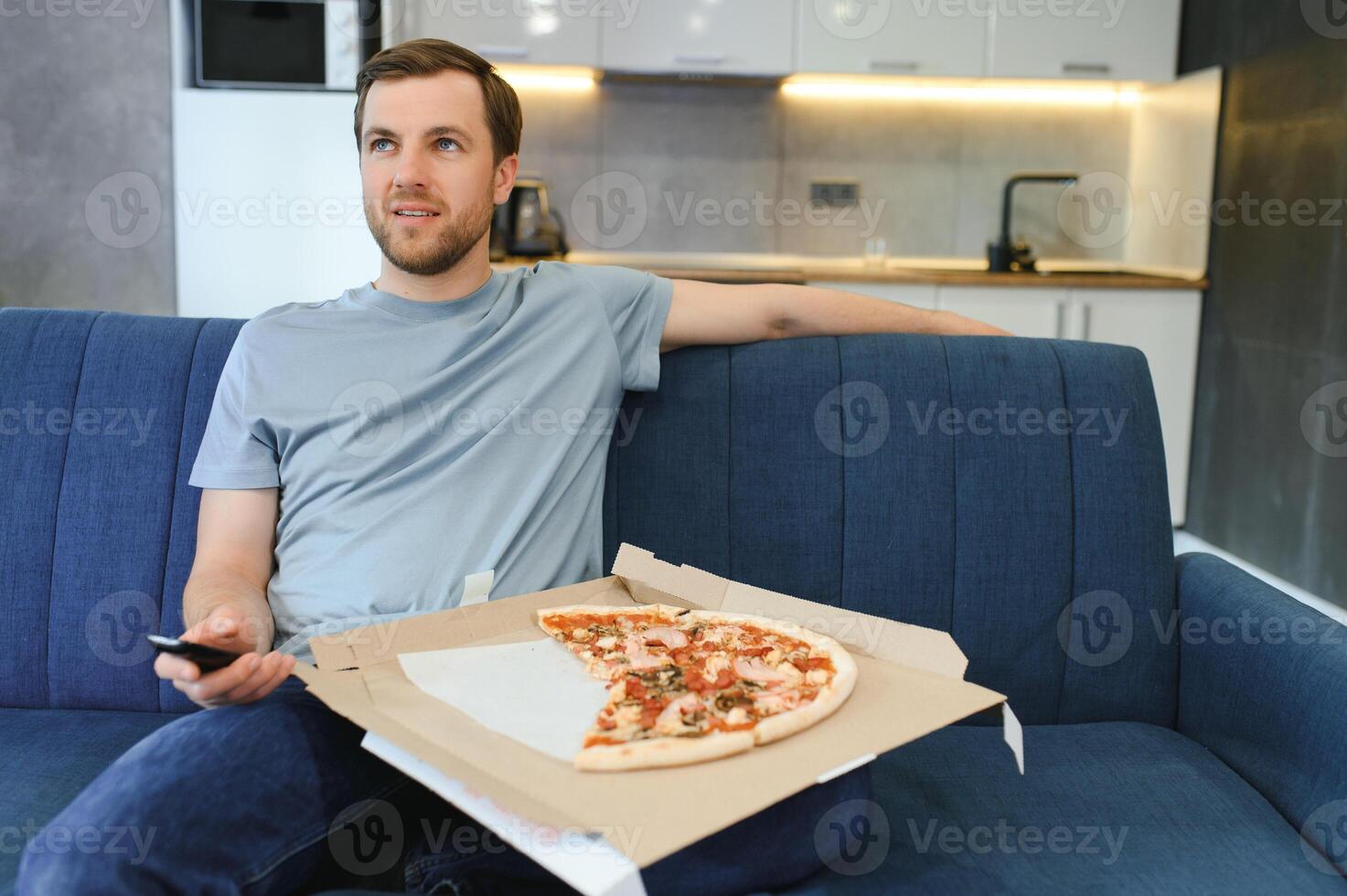 eet pizza terwijl aan het kijken TV show. Mens met baard binnenshuis. foto