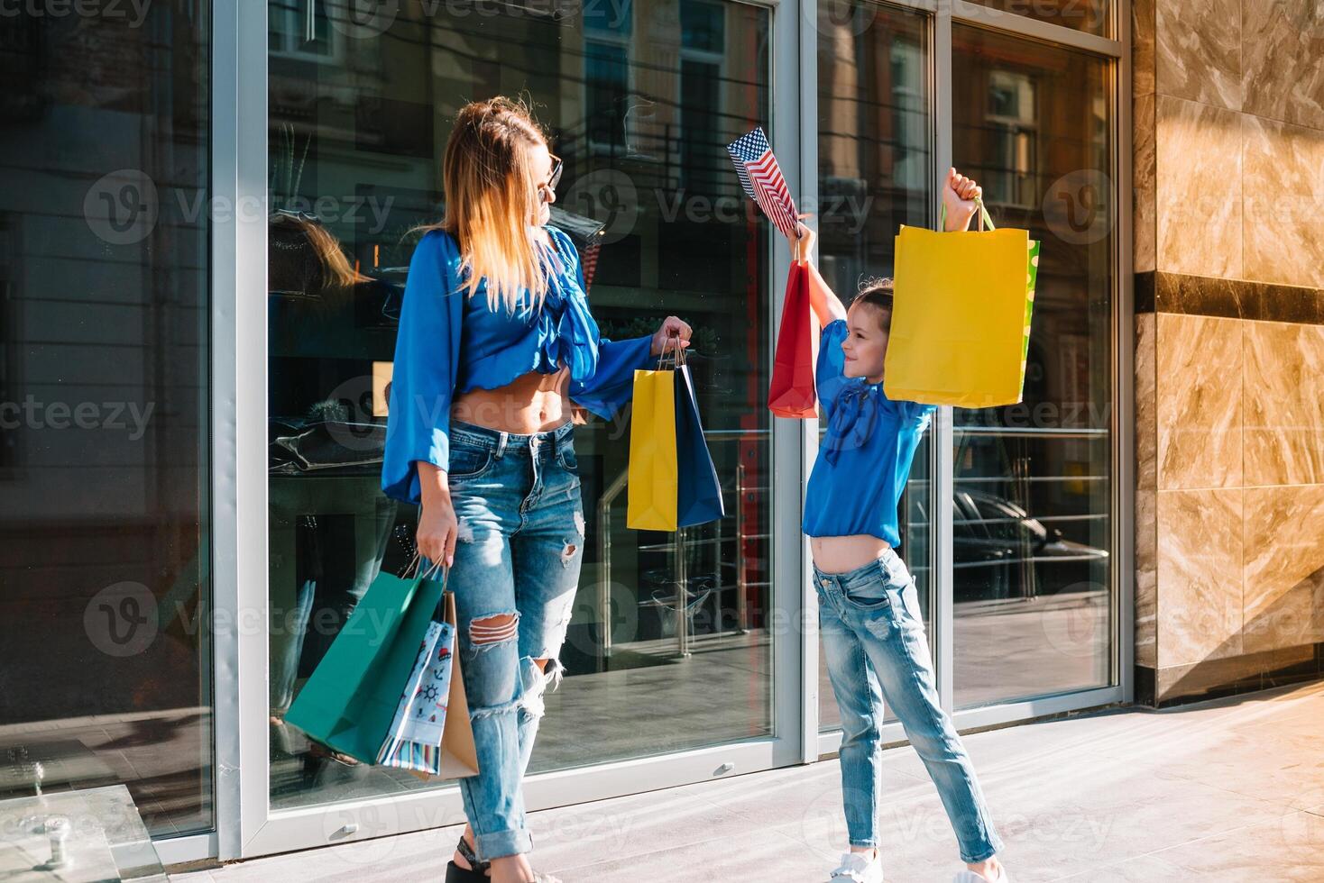 jong moeder en haar dochter aan het doen boodschappen doen samen. vrouw met meisje kind na boodschappen doen in straat. vrouw met dochter met boodschappen doen Tassen buitenshuis. vrouw en haar dochter na winkelen. foto