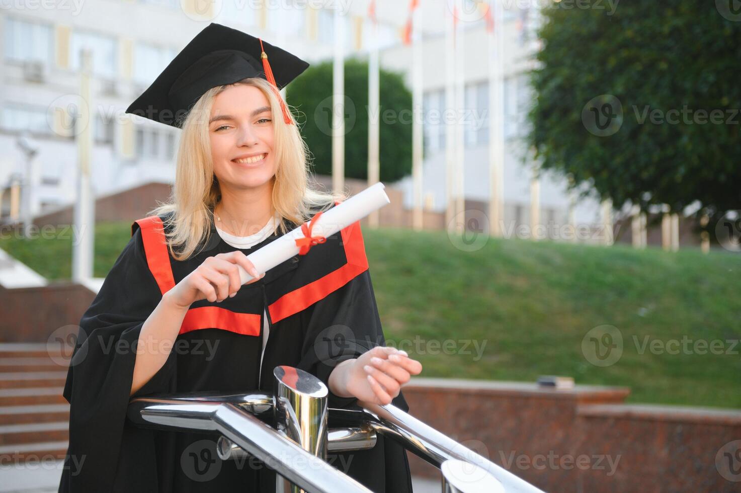 gelukkig schattig Kaukasisch grad meisje is lachend. ze is in een zwart Mortier bord, met rood kwast, in gewaad, met mooi hoor bruin gekruld haar, diploma in hand- foto