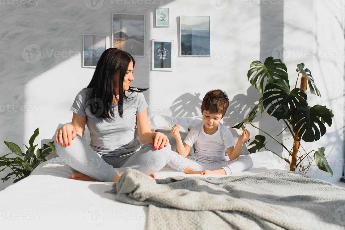 mooi zwanger vrouw en haar schattig weinig baby zoon zijn zittend in lotus positie en glimlachen terwijl mediteren en aan het doen yoga Bij huis foto