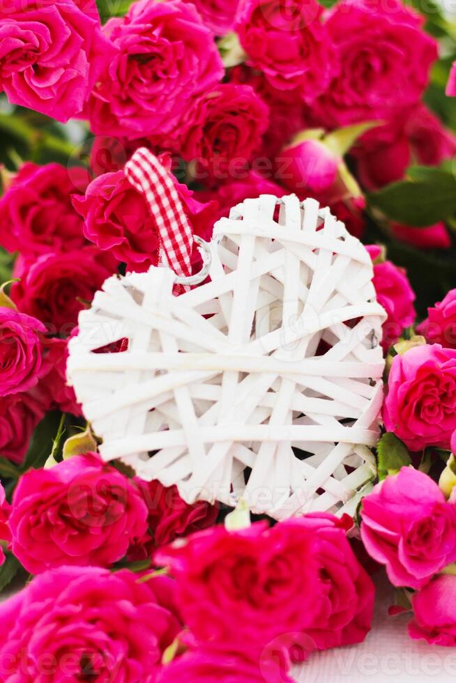 decoratief wit hart gemaakt van wijnstokken, Valentijnsdag dag Aan de achtergrond van een boeket van rozen. foto
