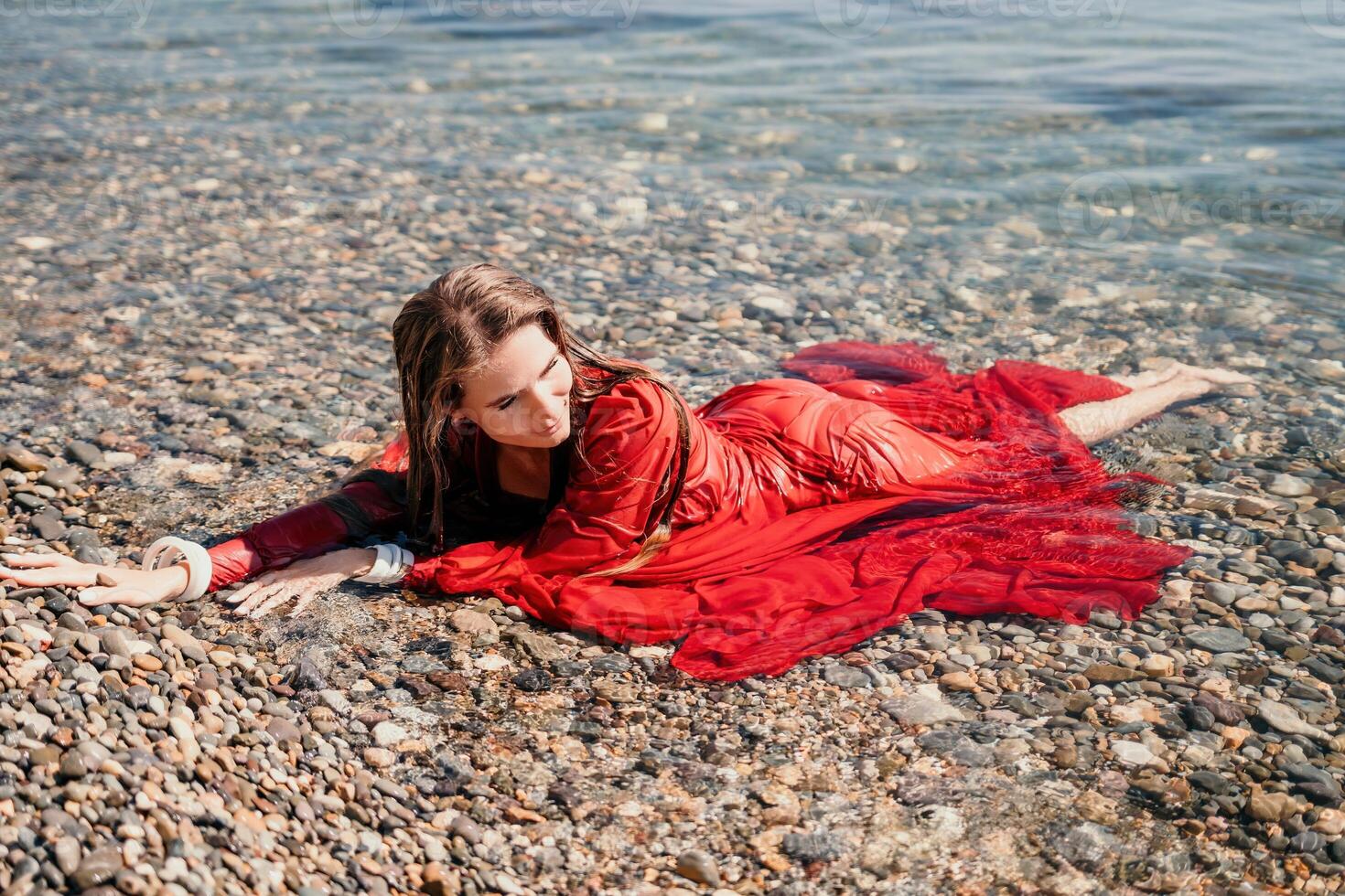 vrouw reizen zee. gelukkig toerist in rood jurk genieten nemen afbeelding buitenshuis voor herinneringen. vrouw reiziger poseren in zee strand, omringd door vulkanisch bergen, sharing reizen avontuur reis foto