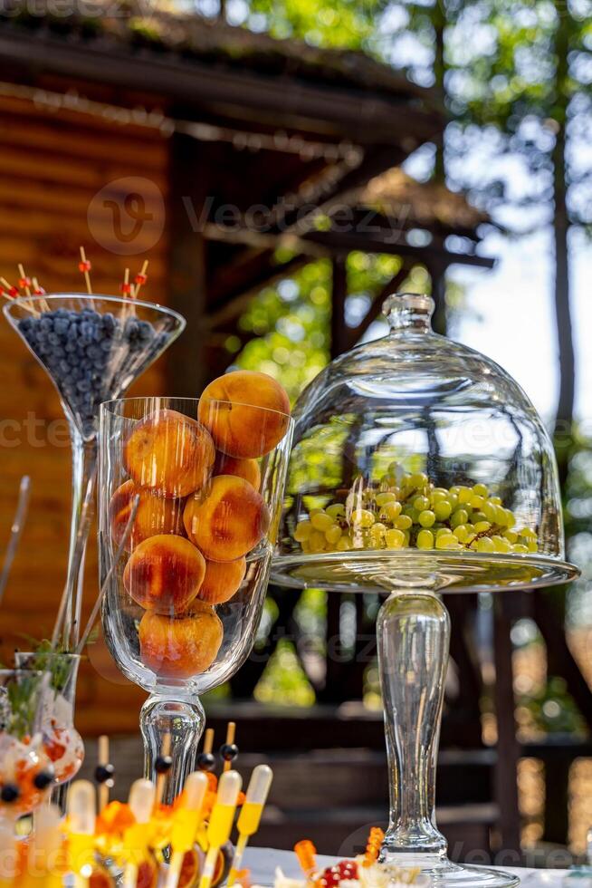 gerechten met bosbessen en perziken. fruit Aan partij tafel. druiven onder glas transparant koepel omslag. toetje Aan de feestelijk tafel. foto