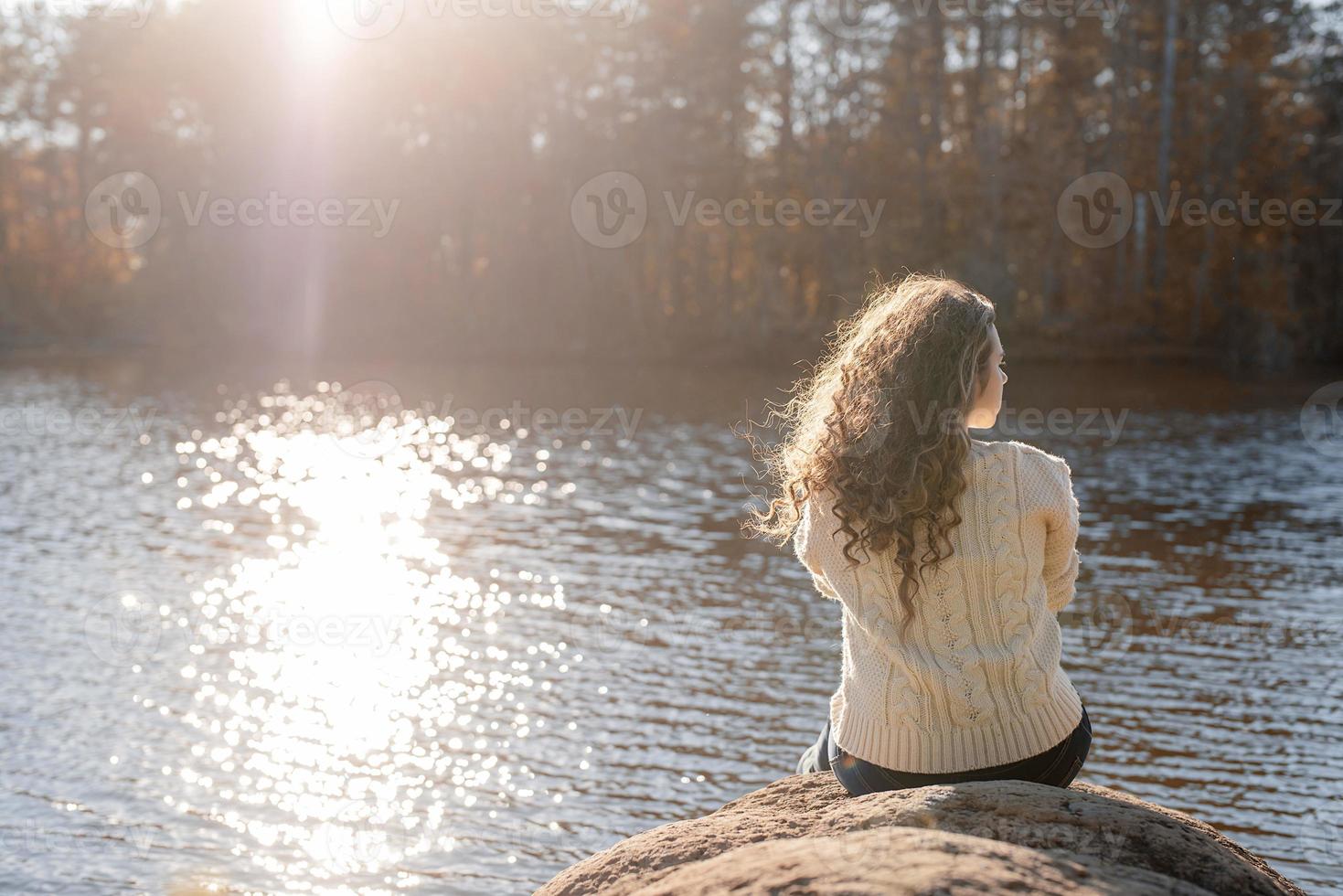 doordachte romantische vrouw zittend op de oever van de rivier bij zonsondergang in de herfstdag foto