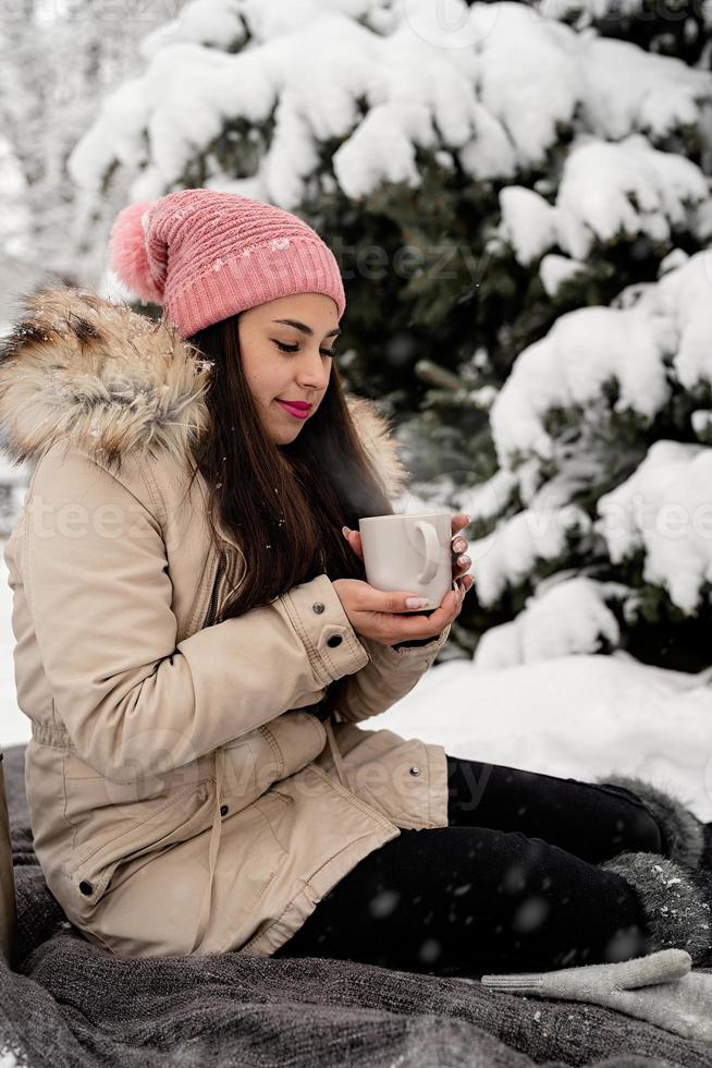 mooie vrouw in warme winterkleren met een kop die hete thee of koffie buiten drinkt op een besneeuwde dag foto