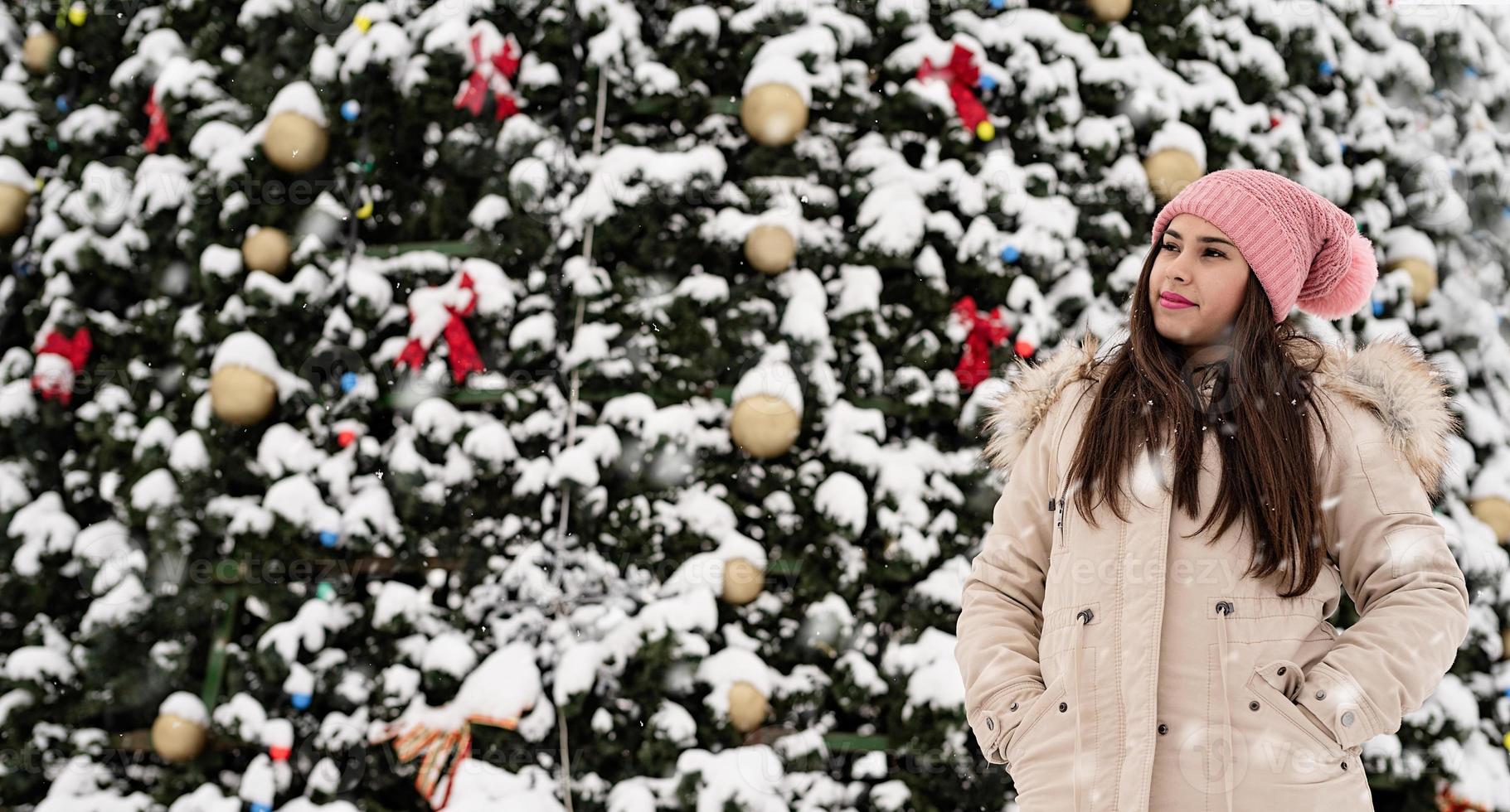 vrouw in warme winterkleren die buiten bij de grote kerstboom staan, sneeuw valt foto