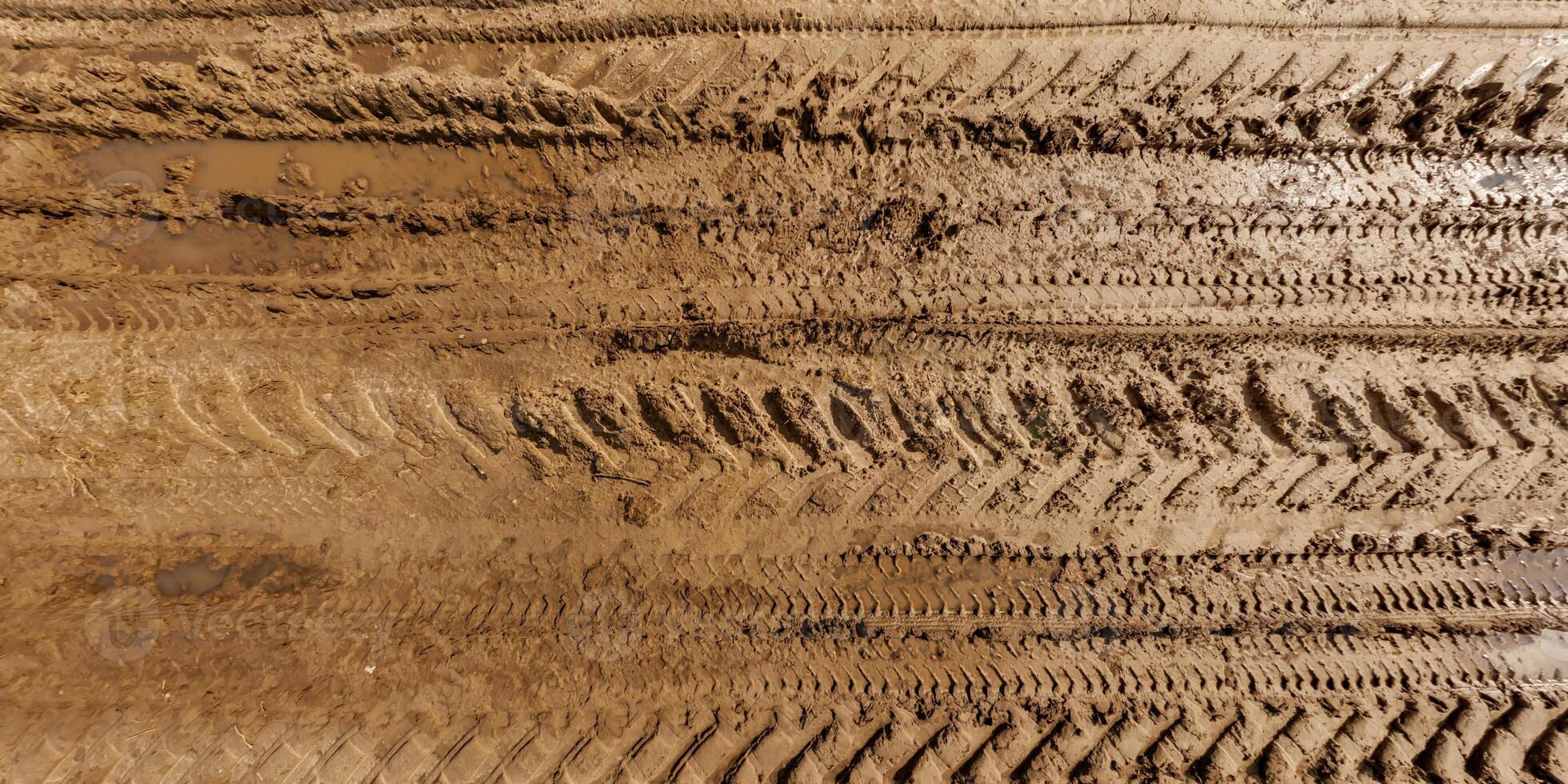 visie van bovenstaand Aan structuur van nat modderig weg met plas en trekker band sporen in platteland foto