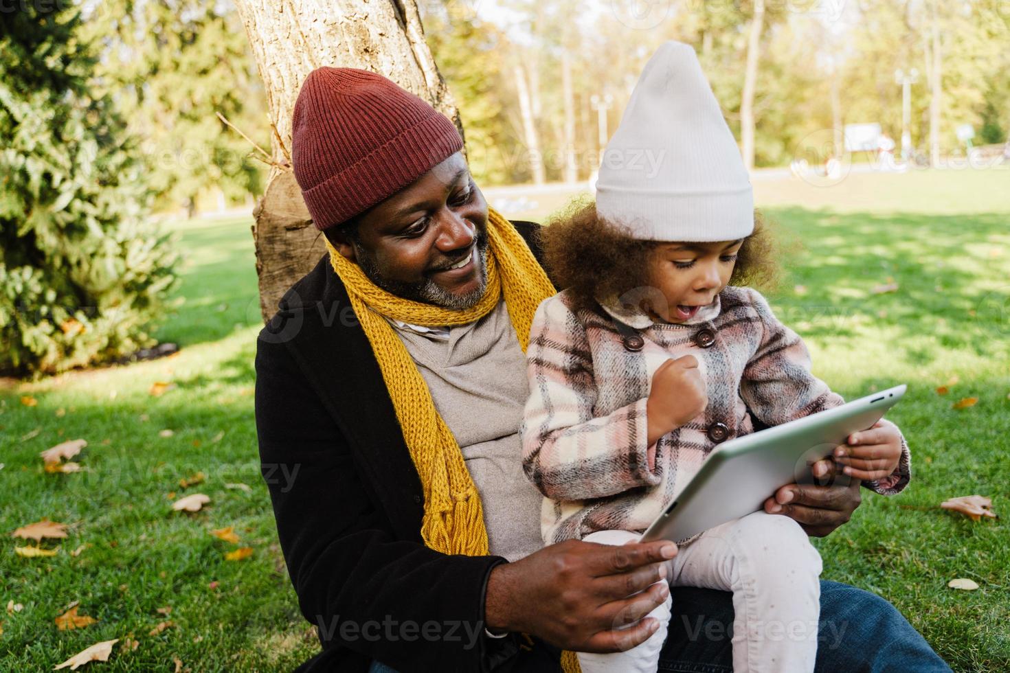 zwarte grootvader en kleindochter die tabletcomputer gebruiken terwijl ze in het park zitten foto