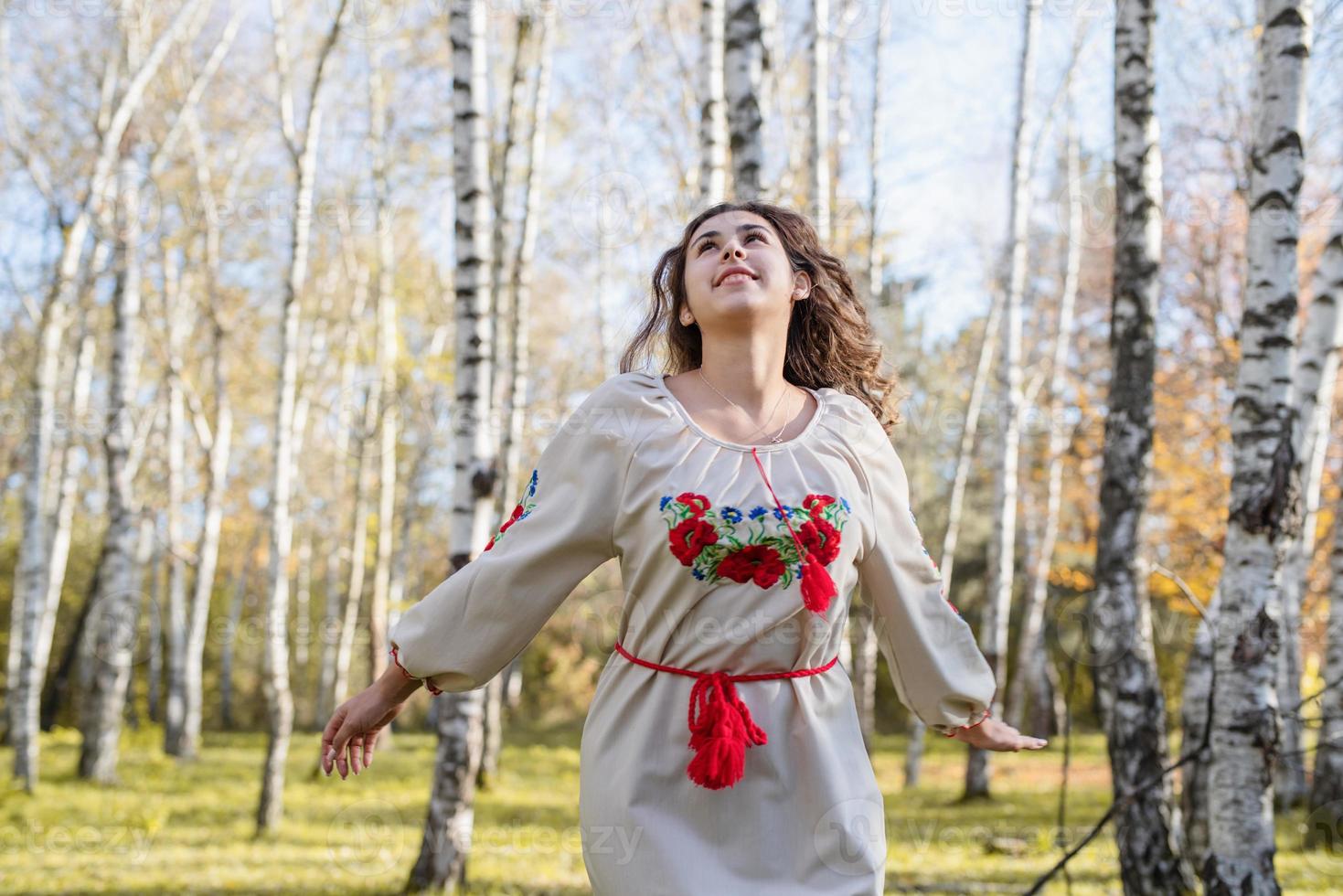 mooie vrouw in Oekraïense nationale traditionele kostuumkleren die in bos dansen foto
