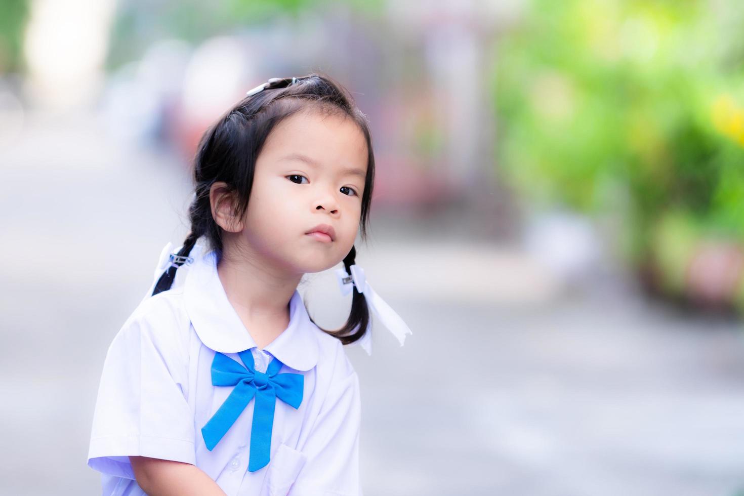 schattig Aziatisch meisje tilt iets op. vrouwelijke student stond te wachten op haar voorbereiding om naar school te gaan. kind is 3 jaar. foto