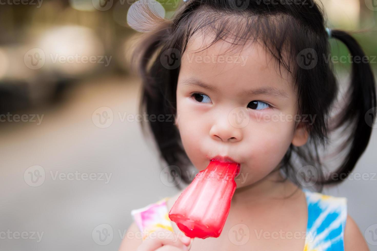 hoofdschot schattig Aziatisch klein kindmeisje dat rood ijs eet. kind van 3 jaar oud. in de zomer of lente. foto