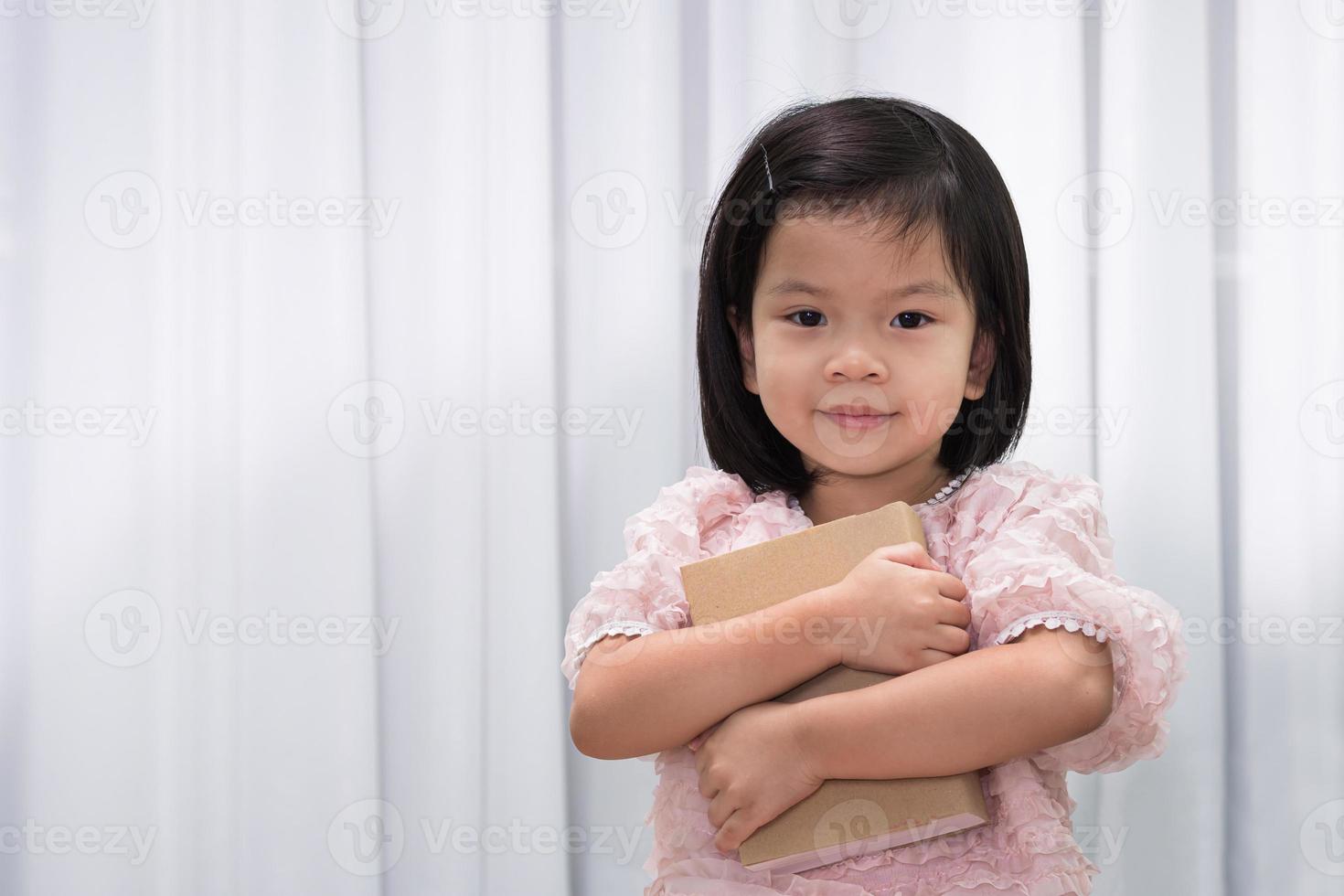 wereldboek en auteursrechtdagconcept. een schattig meisje knuffelt een boek dicht bij haar lichaam. kinderen houden van lezen. schattig kind van 4-5 jaar oud. op witte gordijnachtergrond. opleiding. terug naar school. foto