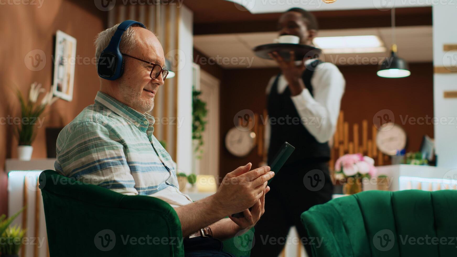 senior volwassen aan het kijken film Aan tablet en genieten van internet streaming Diensten in hotel lobby. toerist gebruik makend van apparaat naar houden omhoog met favoriete TV serie, aan het wachten voor controleren in werkwijze Aan bank. foto