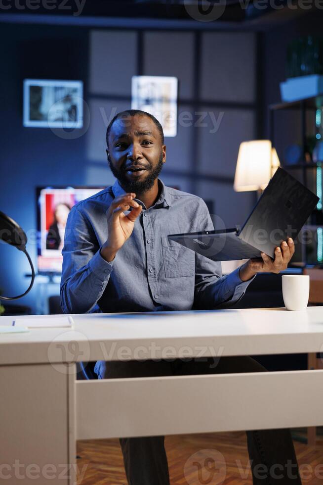 Afrikaanse Amerikaans entertainer presenteren laptop van merk sponsoring video, aandringen op kijkers naar aankoop het. Mens doet influencer afzet door reclame digitaal apparaat naar publiek foto