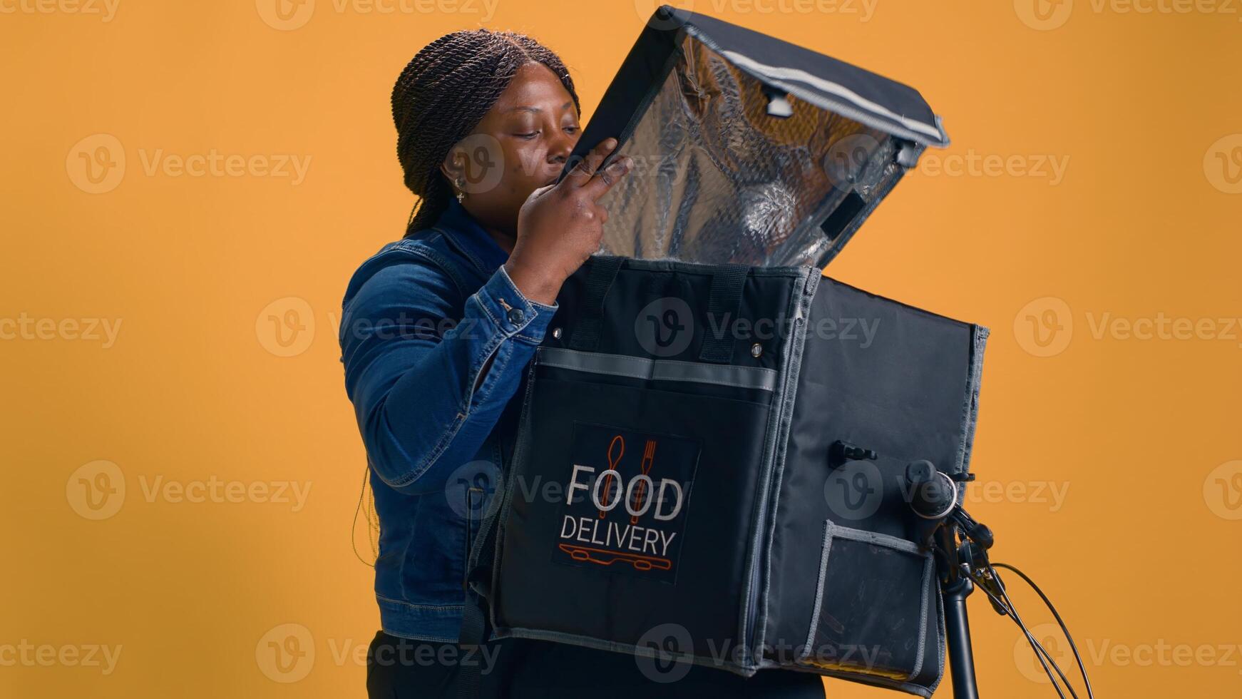 Afrikaanse Amerikaans vrouw verzamelen meenemen van voedsel levering zak voor cliënt. professioneel koerier biedt snel en betrouwbaar klant onderhoud door leveren heerlijk afhaalmaaltijd maaltijden met fiets. foto