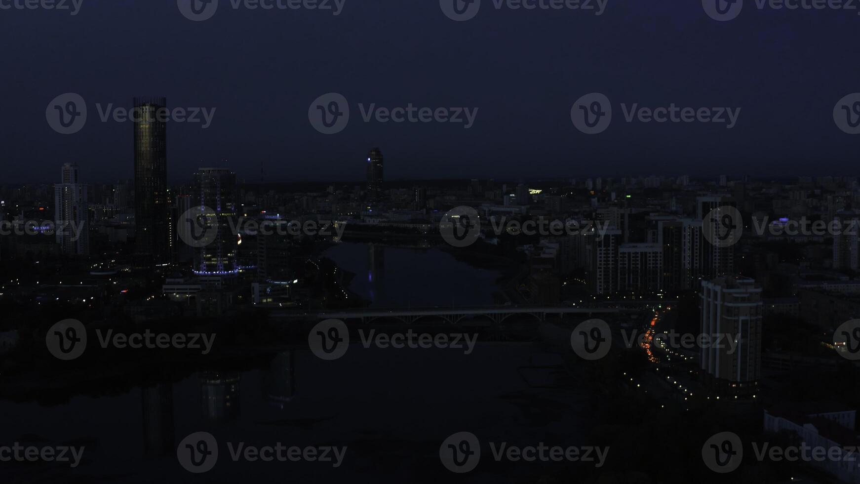 top visie van landschap van avond stad met lantaarns en rivier. voorraad filmmateriaal. mooi panorama van stad met reflectie van zonsondergang licht Aan glas wolkenkrabbers. donker schemering over- gloeiend metropolis foto