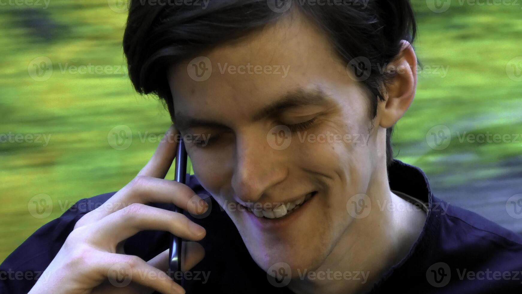 Kaukasisch Mens glimlachen met ogen Gesloten terwijl pratend met iemand Aan de smartphone. voorraad klem. gezicht van een Mens zittend in de buurt de venster in de tram of bus. foto