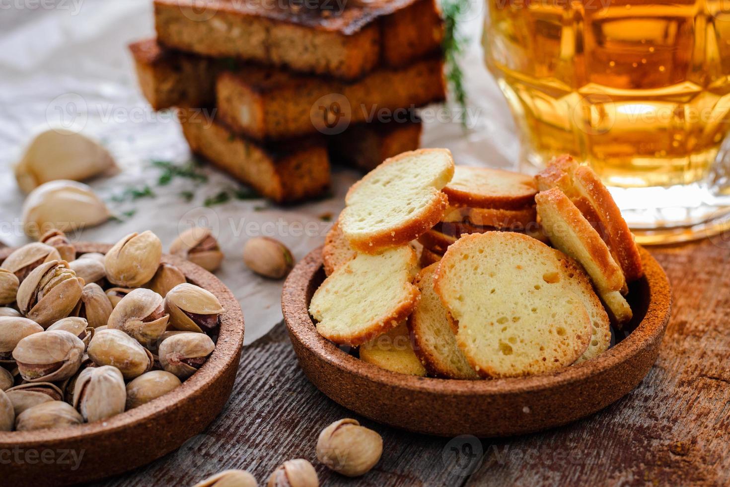 bier in een glas, pistachenoten, roggecroutons en crackers op een houten tafel foto