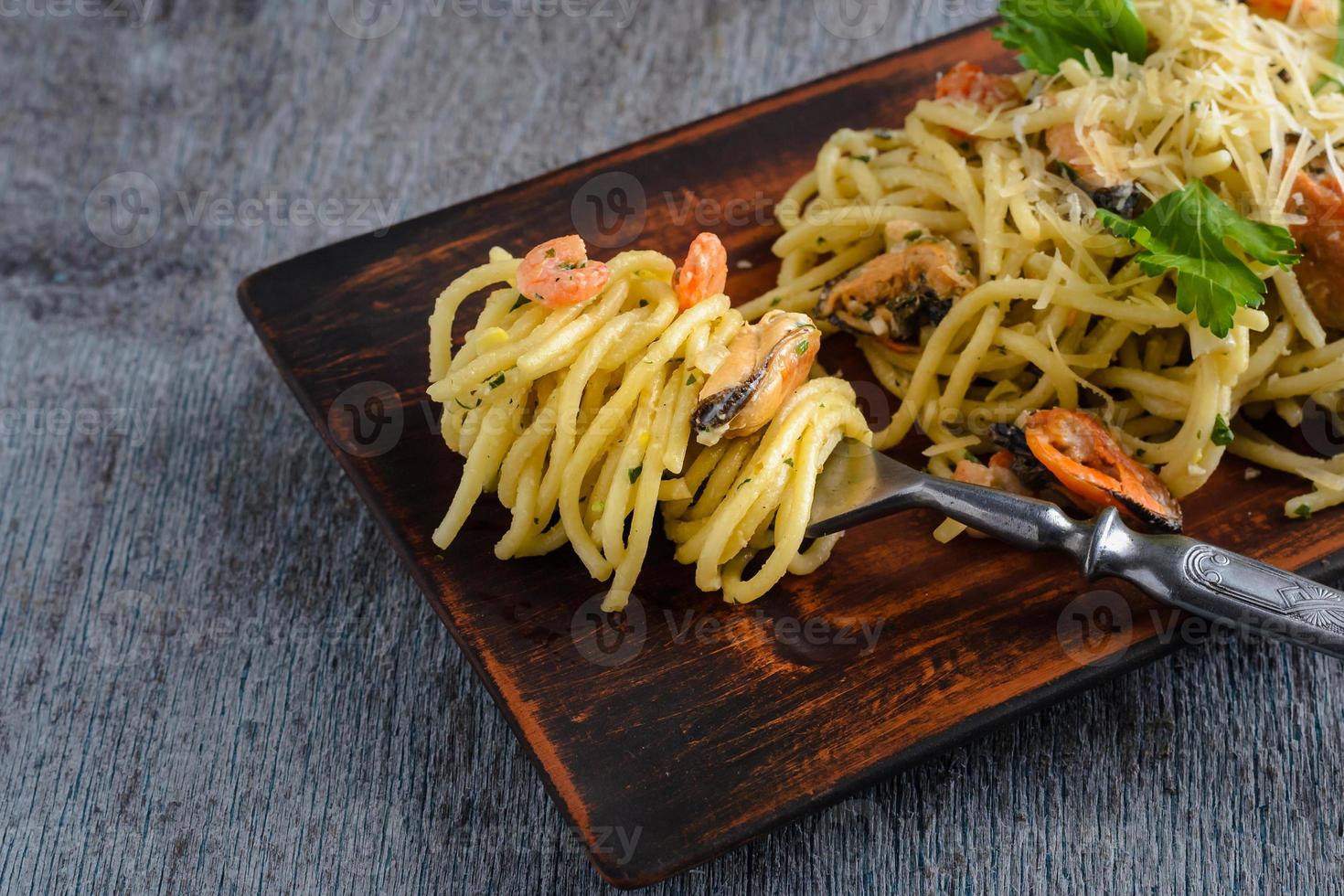 pasta in een romige saus met zeevruchten, garnalen en mosselen in een kleiplaat op een donkere houten ondergrond foto