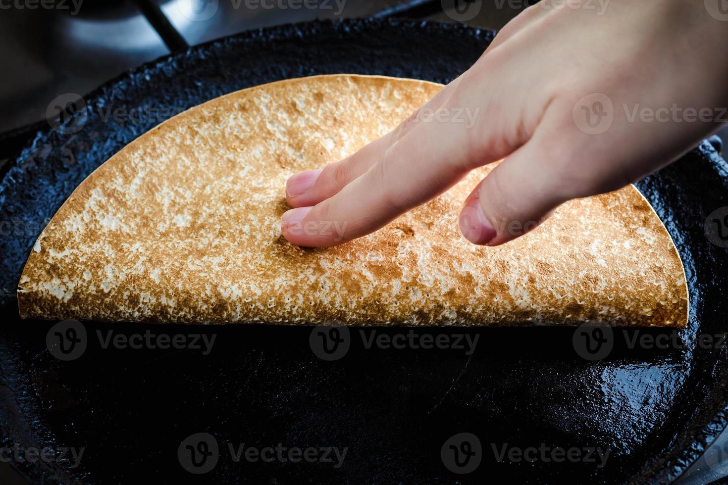 jonge vrouw quesadilla bakken in een koekenpan foto