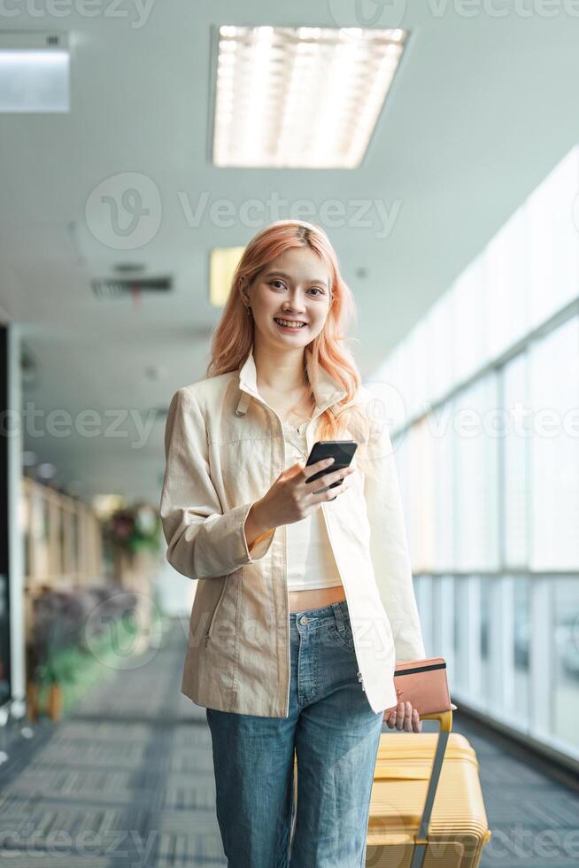 reiziger vrouw Aziatisch in luchthaven en bagage voor vakantie, glimlach en Holding de telefoon controleren instappen ticket. vrouw reiziger met koffer, Internationale en vertrek met paspoort en reis foto