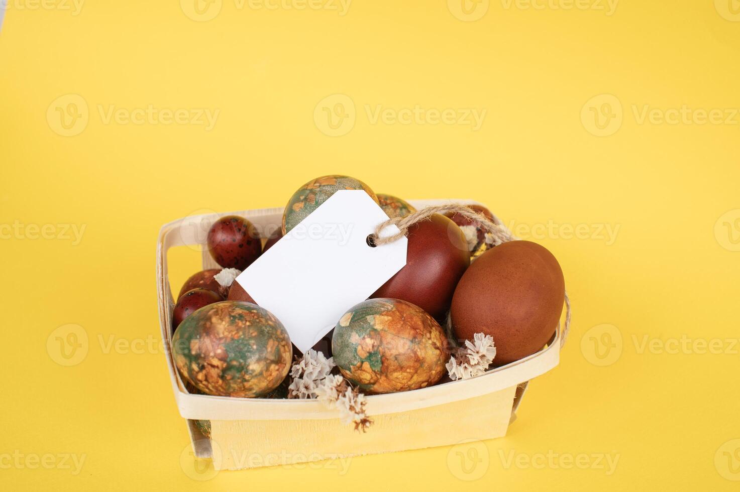 Pasen eieren met gevarieerd natuurlijk patronen in een klein houten mand met een blanco label foto