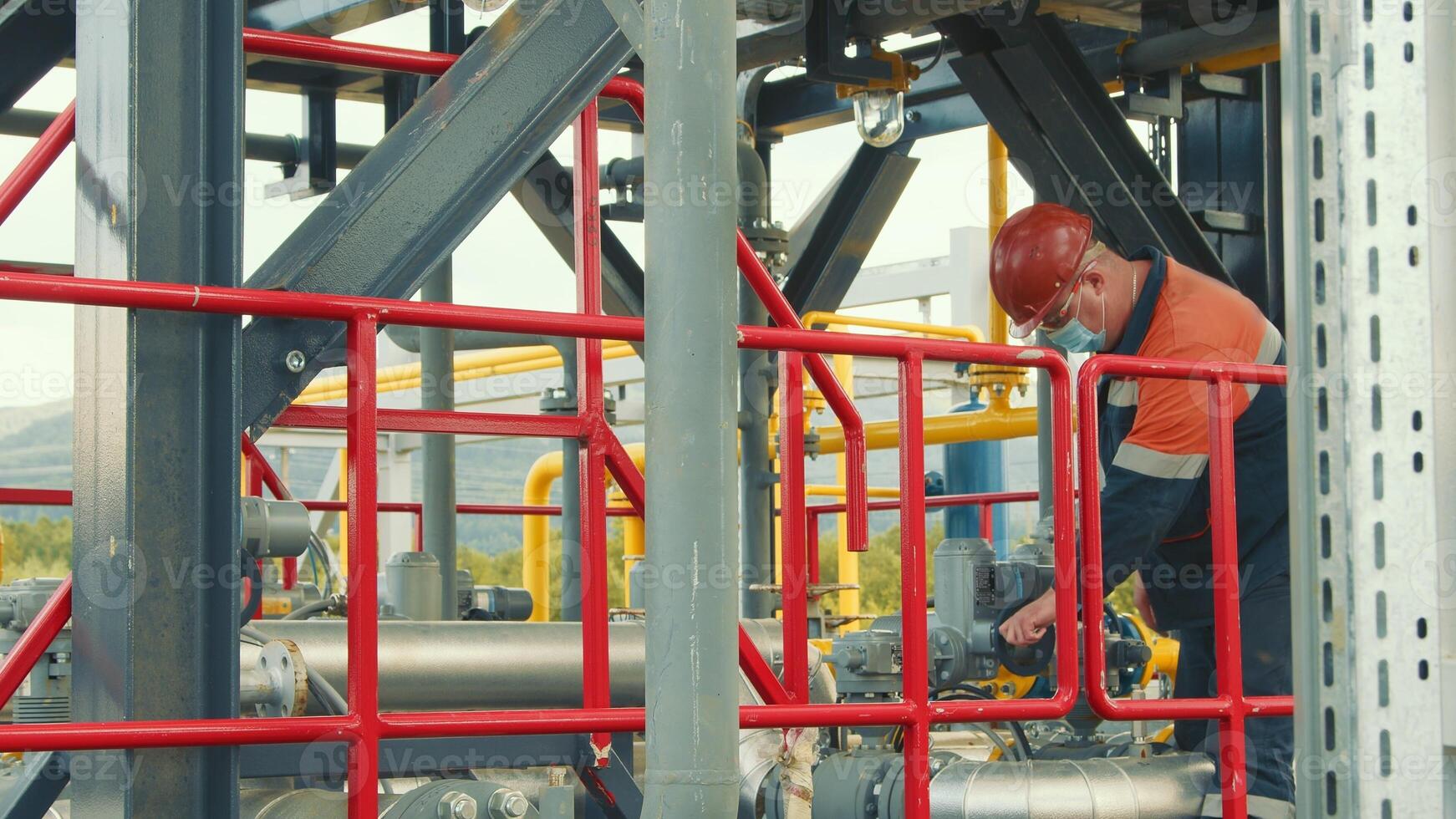 werknemer van de gas- station in een beschermend medisch masker, gas- distributie station bochten of draait los de gas- levering ventiel. werk van een gas- productie arbeider Bij een gas- station. foto