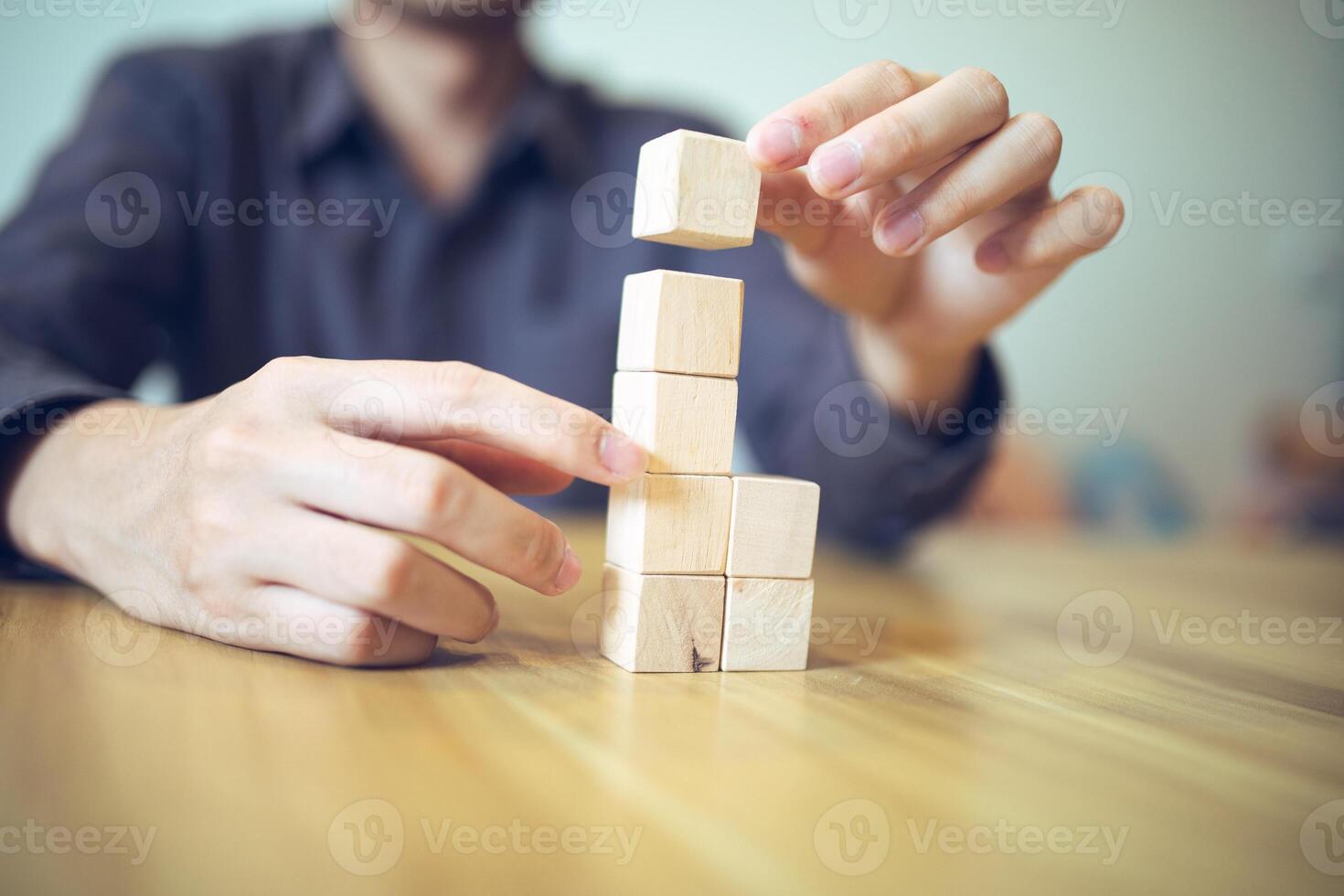 hand- strategisch plaatsen houten blokken in een traptrede ontwerp Aan een tafel, betekenend progressief succes en groei foto