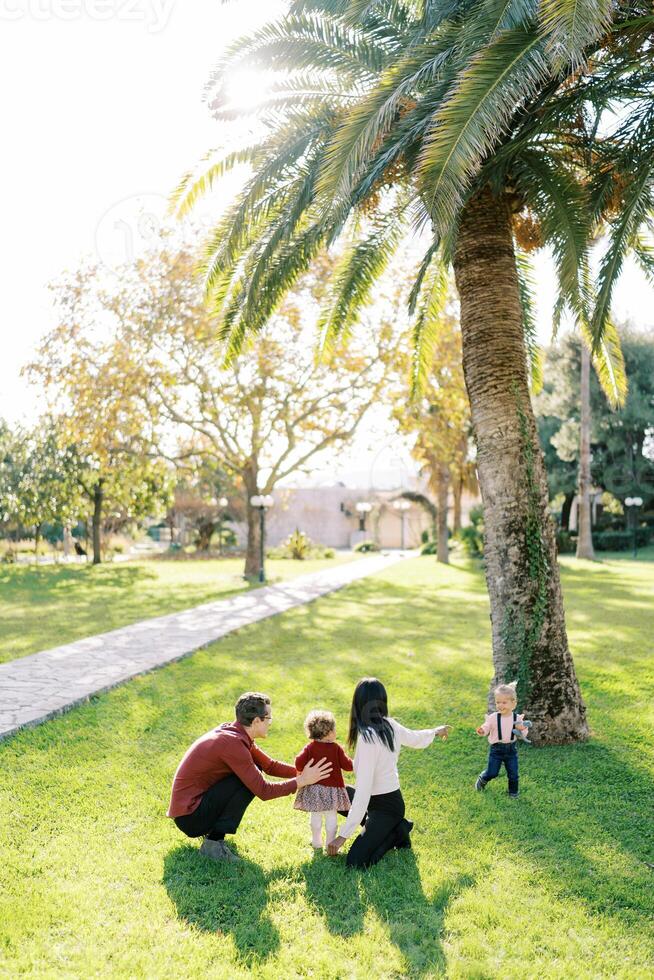 ouders met een weinig dochter gehurkt in de park in voorkant van een klein meisje foto