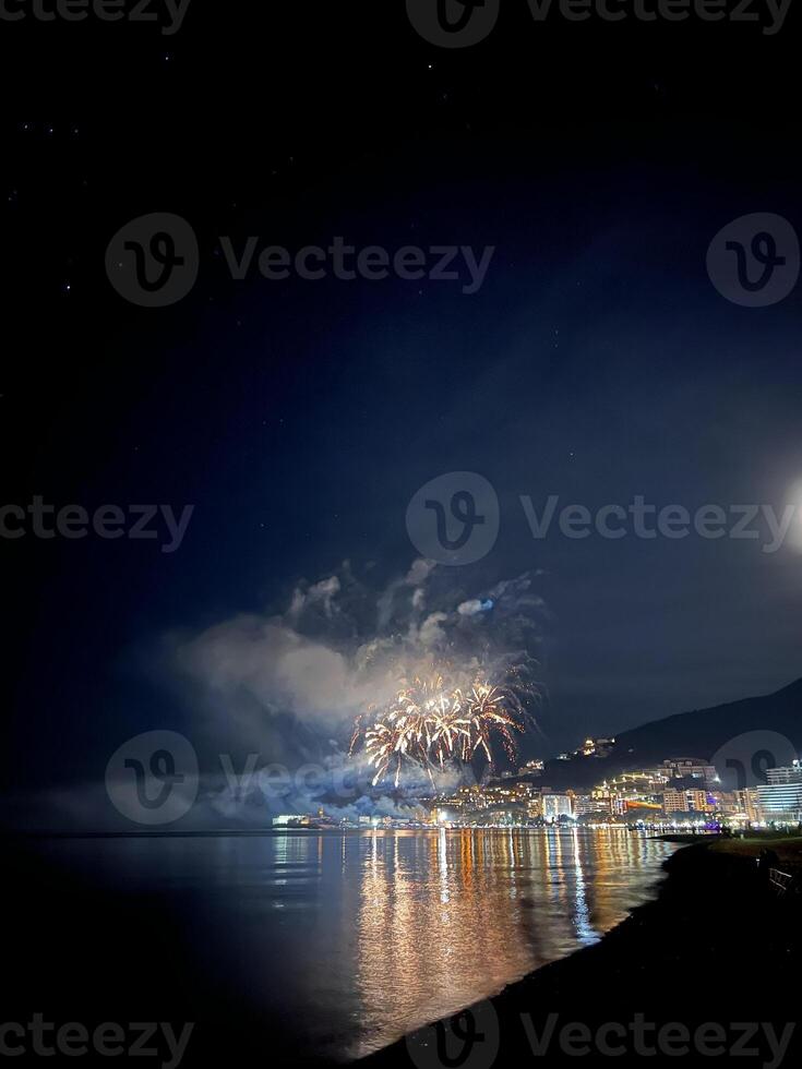 feestelijk vuurwerk in de donker lucht over- de verlichte stad- door de zee foto