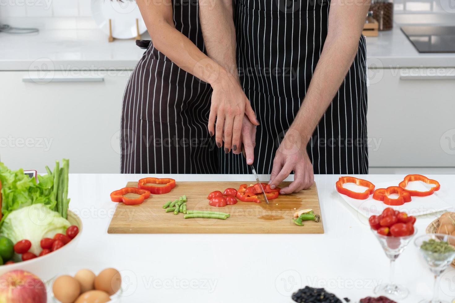 jonge vrouw die de hand van de man vasthoudt om groente te hakken om de lunch in de keuken te bereiden. koppel samen concept foto