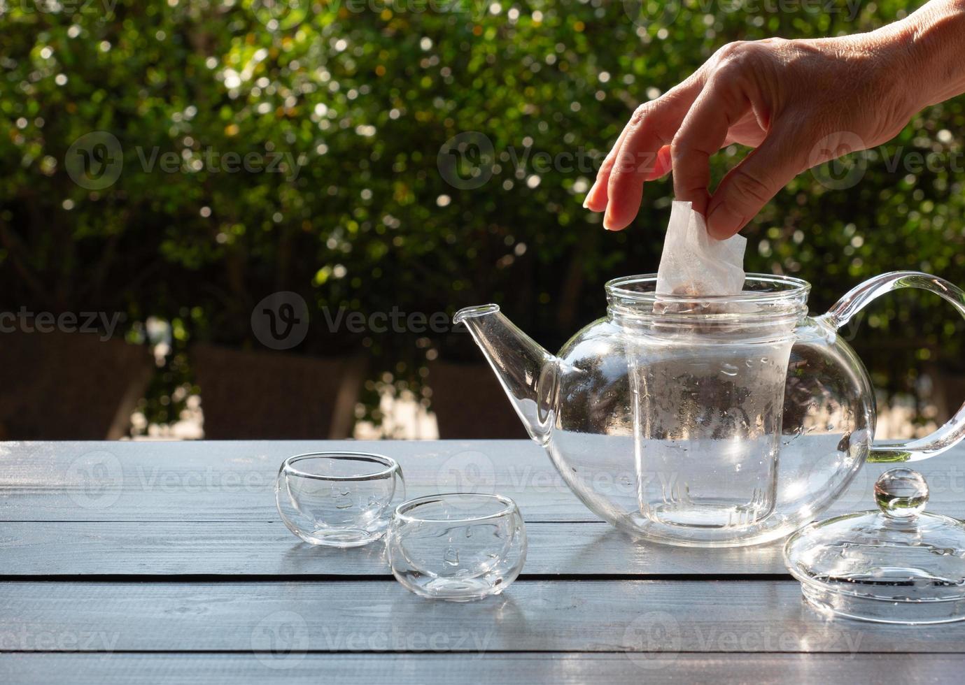 oudere mensen doen een theezakje in een glazen waterkoker om hete middagthee in de tuin te maken foto