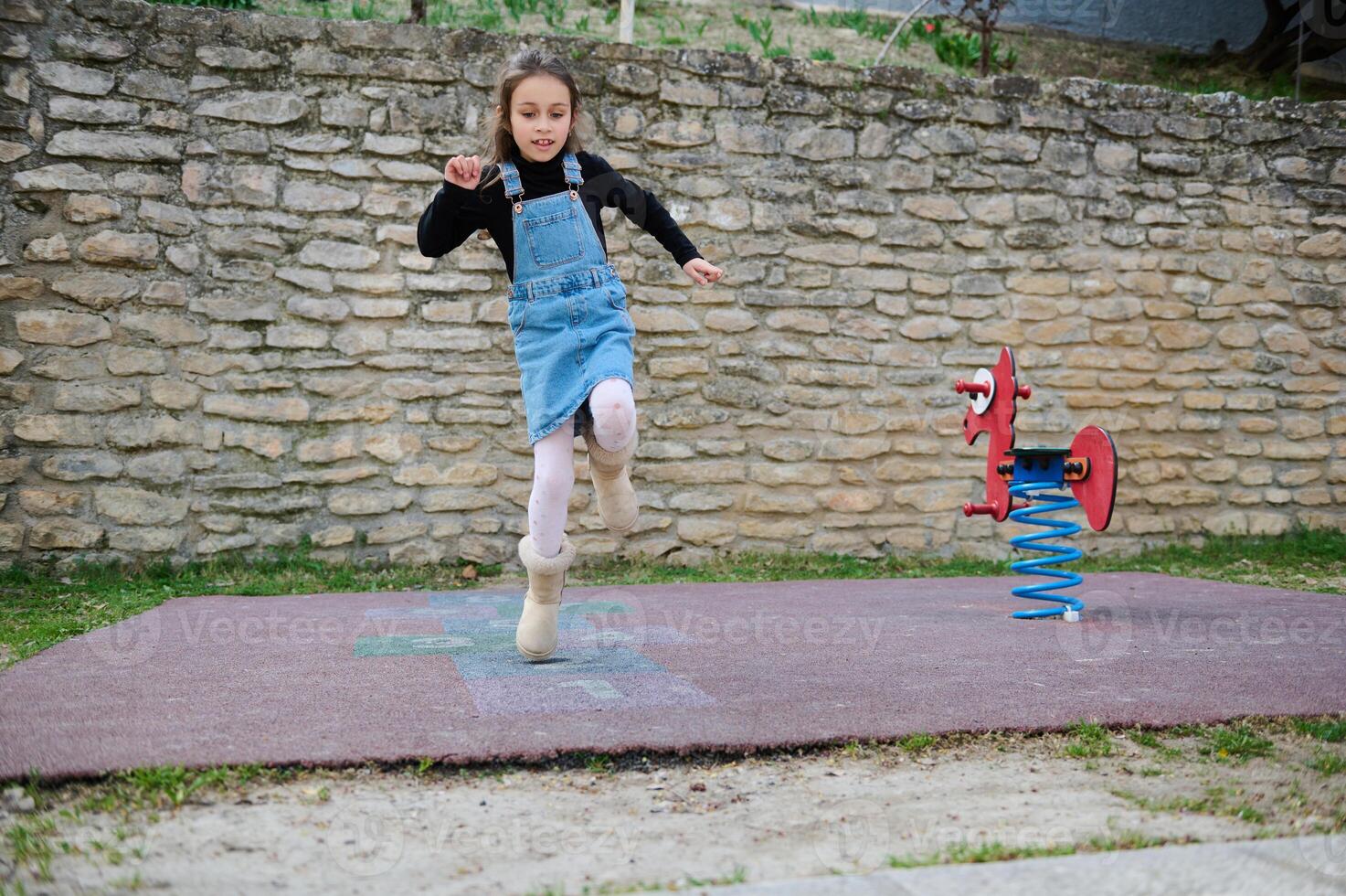 een weinig kind meisje jumping Aan een been, spelen hinkelen Aan een stedelijk speelplaats buitenshuis. hinkelen populair straat spel foto