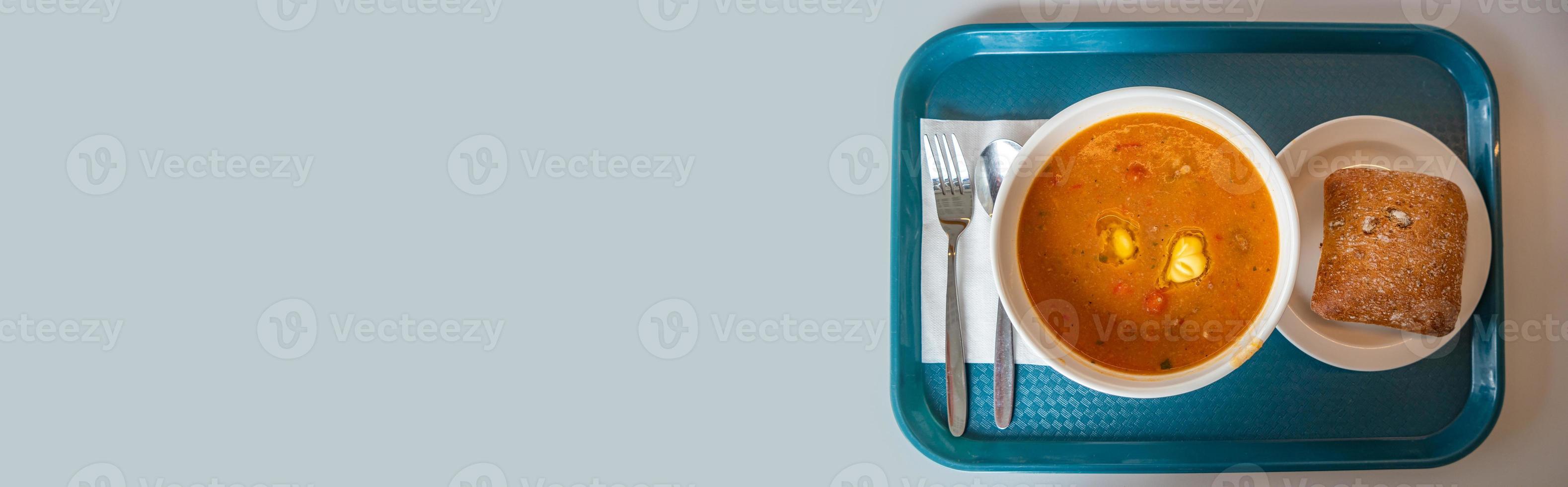 banner met heerlijke en smakelijke soep met groenten, tomaat en vlees, zelfgebakken brood, geserveerd op een dienblad met vork en lepel met lichtblauwe gladde achtergrond voor kopieerruimtetekst, details foto