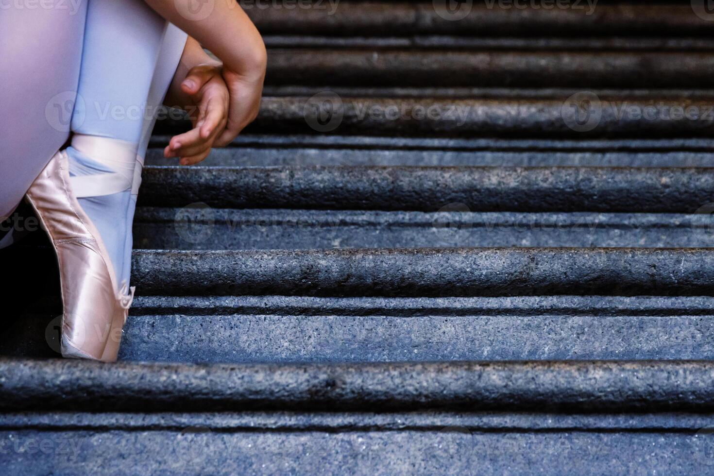 detailopname van ballerina vervelend pointes schoenen Holding haar handen Aan haar enkels terwijl zittend Aan de grijs steen stappen. dans resting Aan de trap. dansers voeten met roze ballet slippers Aan. kopiëren ruimte foto