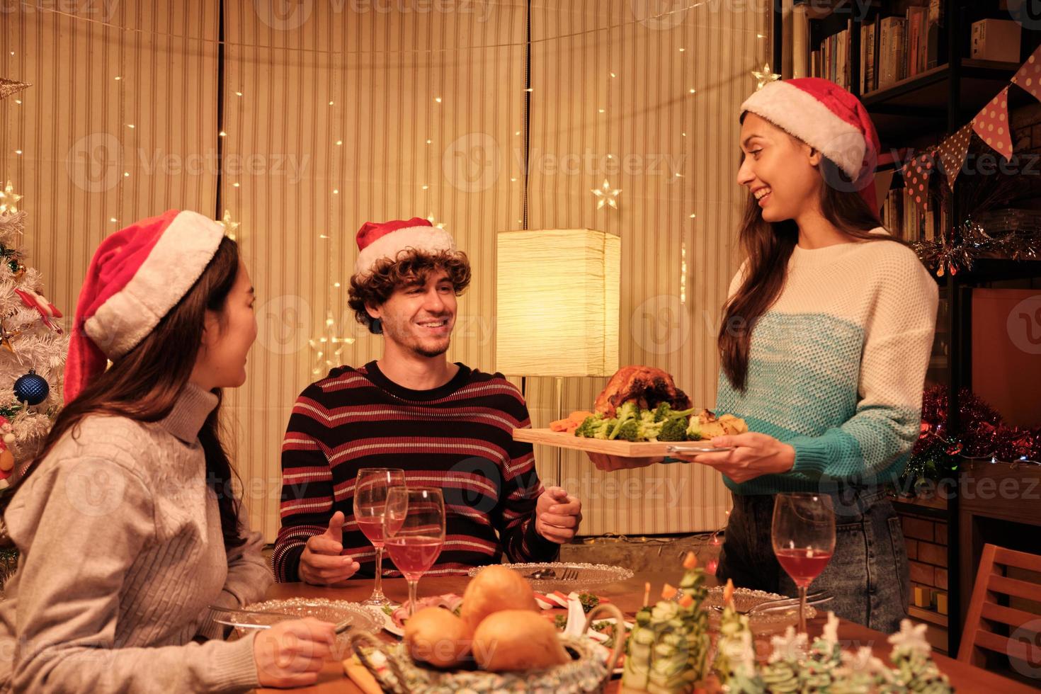 een speciale familiemaaltijd, jonge vrouw serveert geroosterde kalkoen aan vrienden en vrolijk met drankjes tijdens een diner in de eetzaal van het huis die is ingericht voor kerstfestival en nieuwjaarsfeest. foto