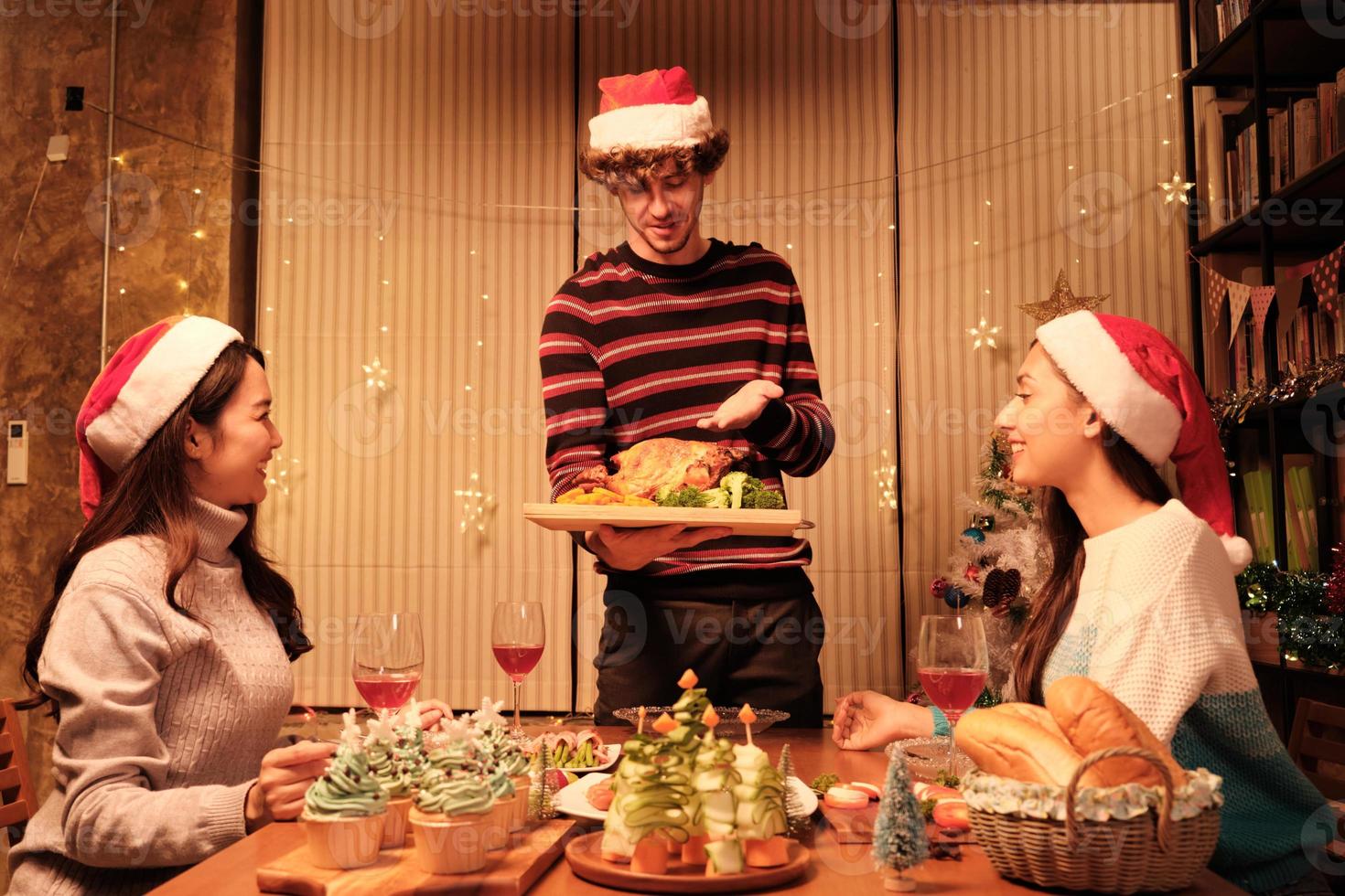 familie's speciale maaltijd, jonge man serveert geroosterde kalkoen aan vrienden, vrolijk met drankjes en geniet van eten, diner in de eetzaal van het huis ingericht voor kerstfestival en nieuwjaarsfeest. foto