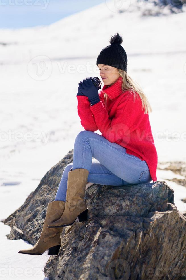 blonde vrouw zittend op een rots in de besneeuwde bergen in de winter, in sierra nevada, granada, spanje. foto