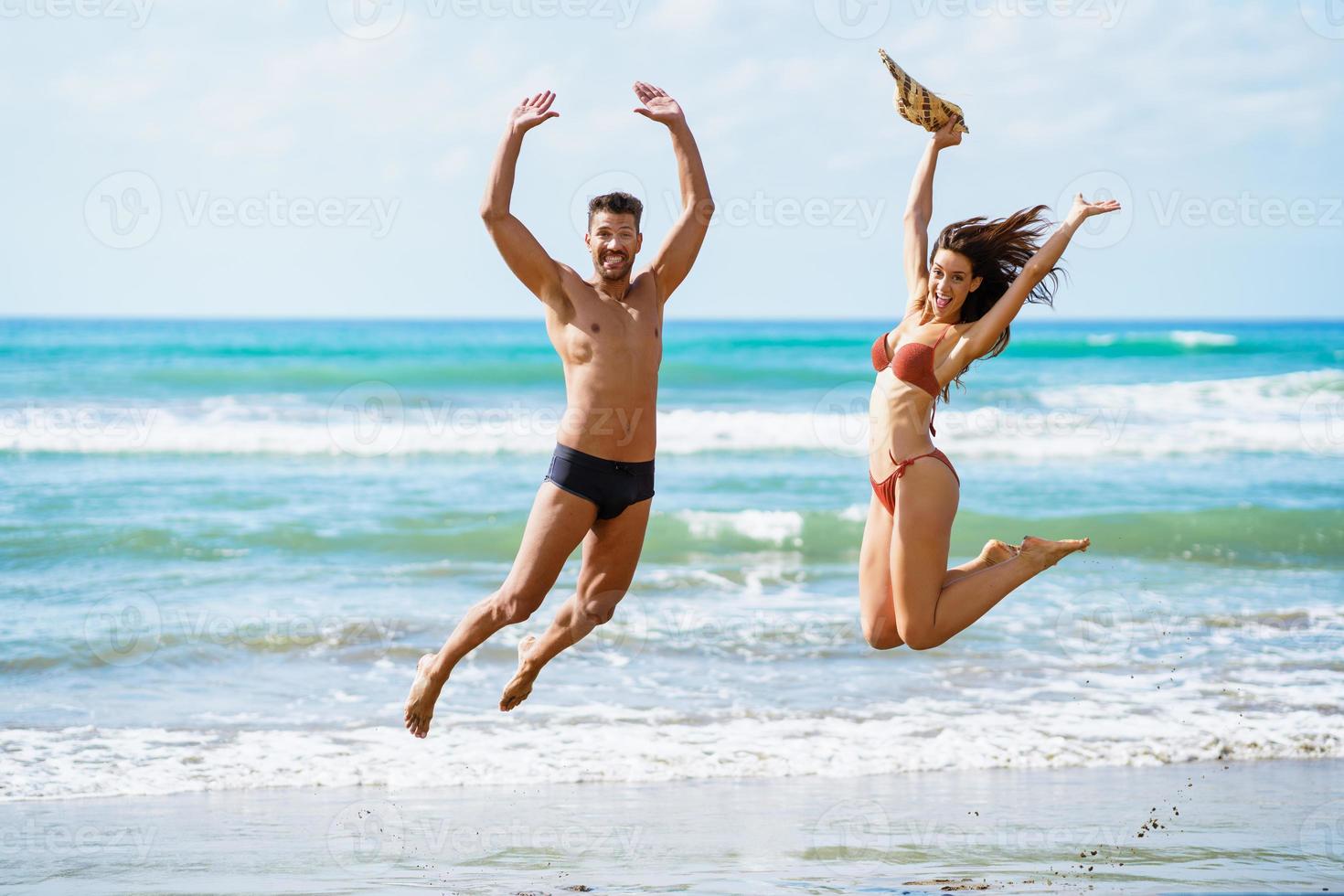 grappig jong stel met mooie lichamen springen op een tropisch strand. foto