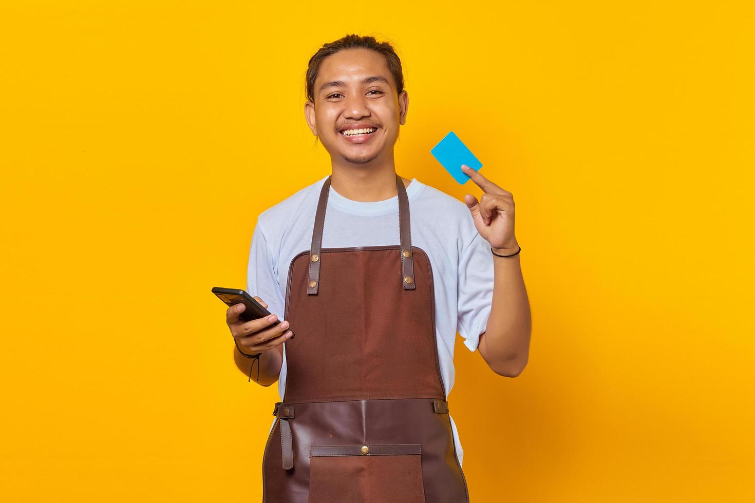 portret van glimlachende knappe barista die creditcard toont om te betalen en smartphone vast te houden foto