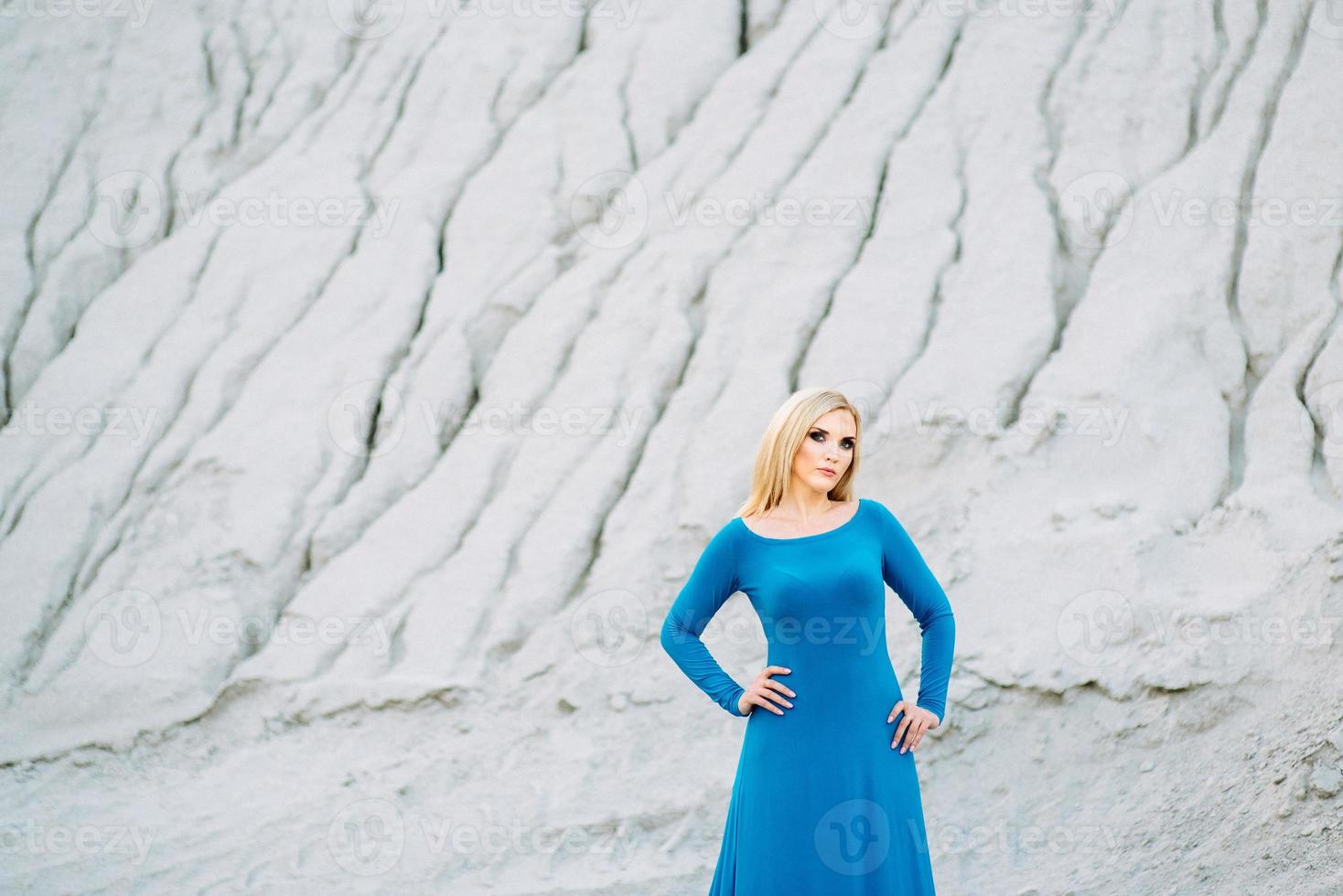 blond meisje in een blauwe jurk met blauwe ogen in een granietgroeve foto