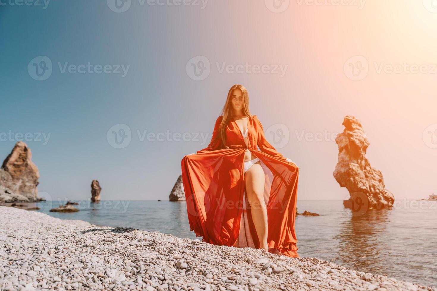 vrouw reizen zee. gelukkig toerist in rood jurk genieten nemen afbeelding buitenshuis voor herinneringen. vrouw reiziger poseren Aan de rots Bij zee baai omringd door vulkanisch bergen, sharing reizen avontuur reis foto