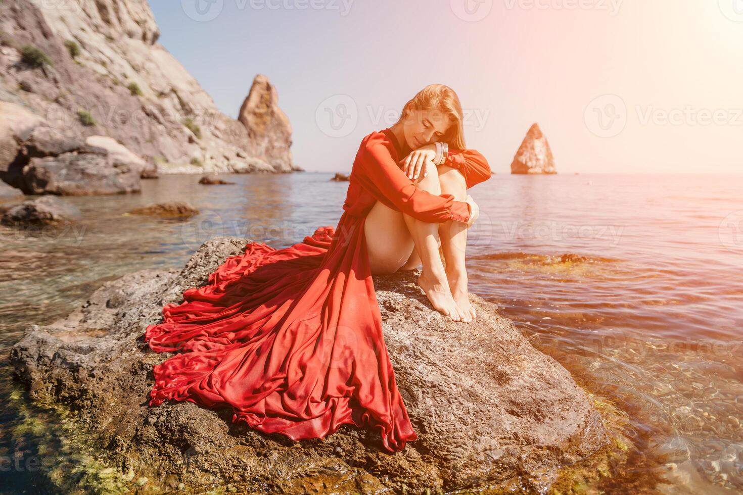 vrouw reizen zee. gelukkig toerist in rood jurk genieten nemen afbeelding buitenshuis voor herinneringen. vrouw reiziger poseren Aan de rots Bij zee baai omringd door vulkanisch bergen, sharing reizen avontuur reis foto
