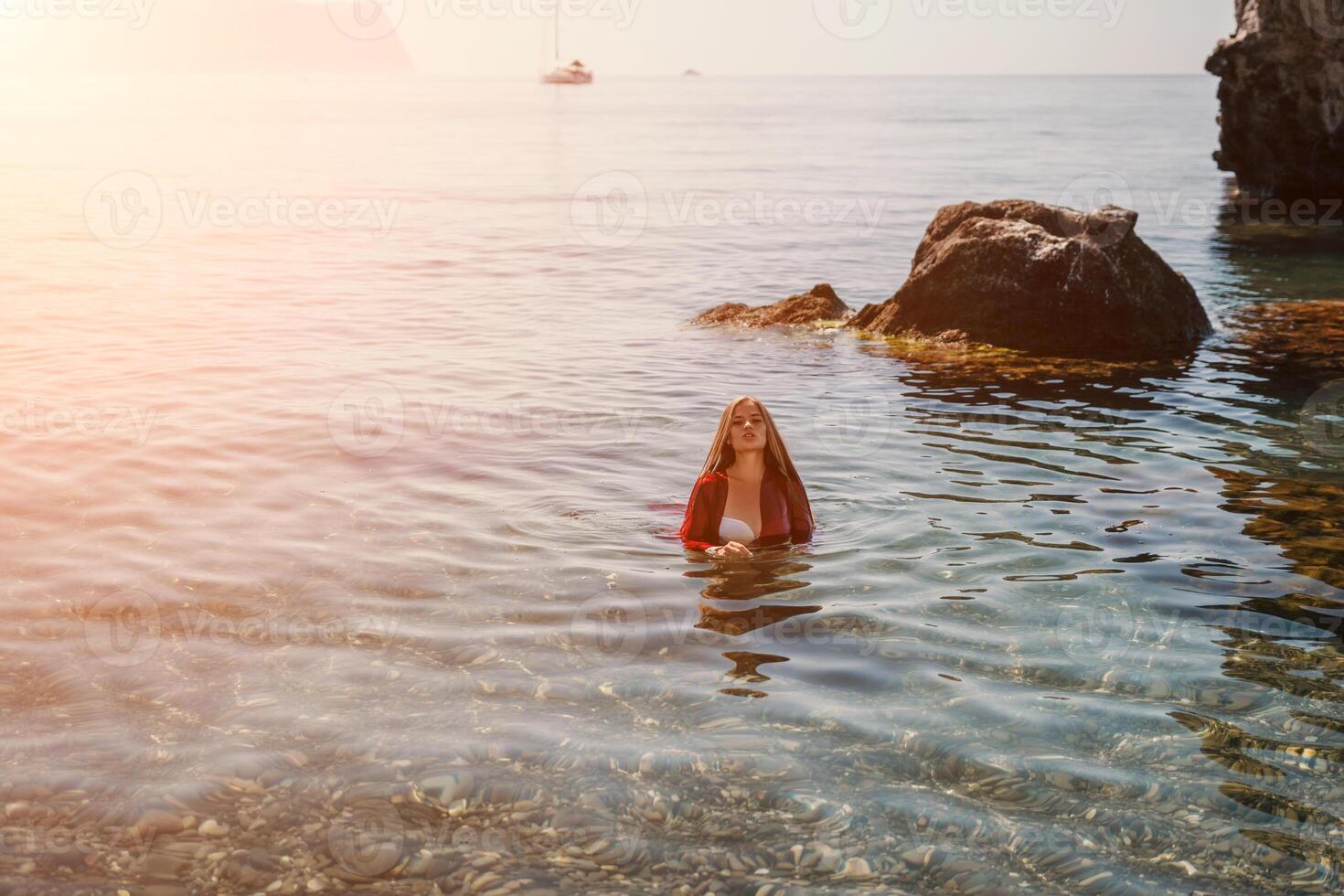 vrouw reizen zee. gelukkig toerist in rood jurk genieten nemen afbeelding buitenshuis voor herinneringen. vrouw reiziger poseren in zee strand, omringd door vulkanisch bergen, sharing reizen avontuur reis foto