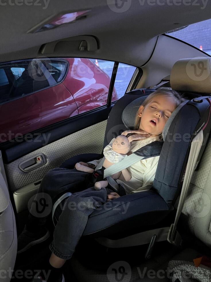 weinig meisje slaapt in een baby auto stoel in de terug stoel van een auto met een pluche konijn foto