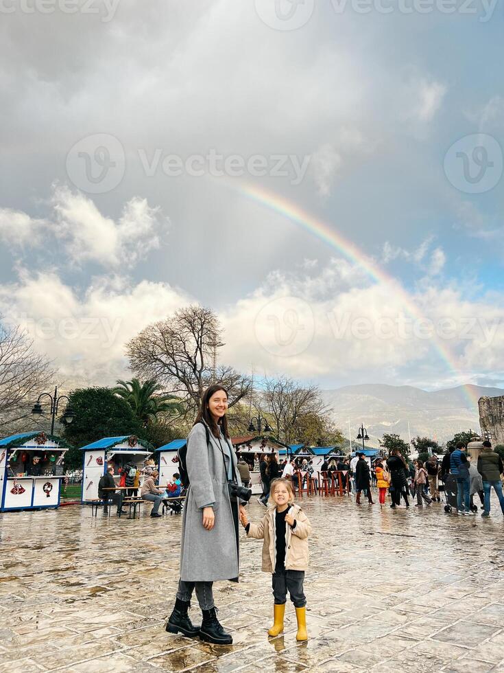 mam met een weinig meisje zijn staand in de buurt de markt tegen de backdrop van een regenboog over- de bergen foto
