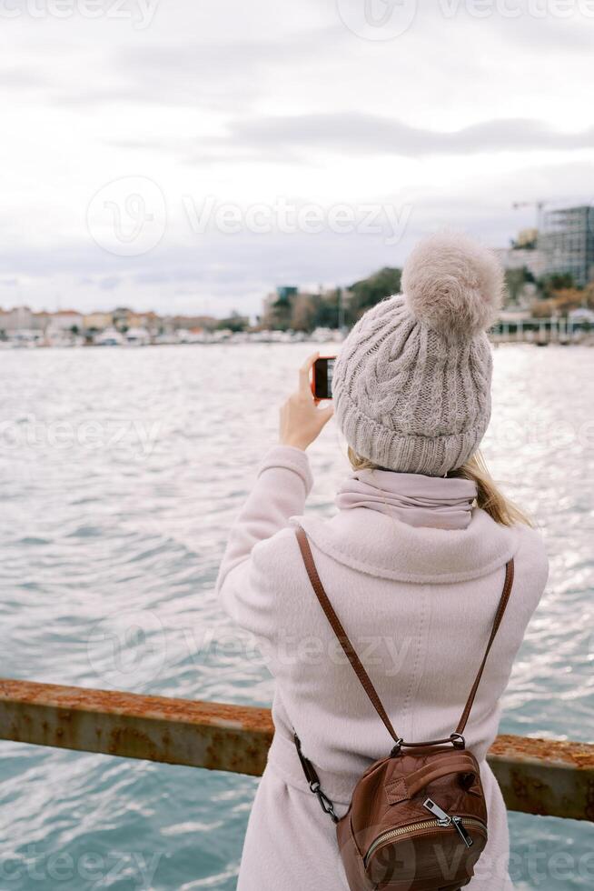 meisje met een rugzak staat Aan de pier en duurt afbeeldingen van de zee kust. terug visie foto