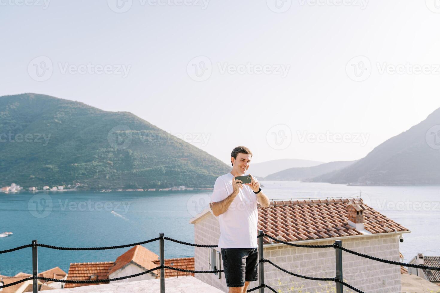 Mens schiet met een smartphone terwijl staand Aan een platform bovenstaand de zee foto