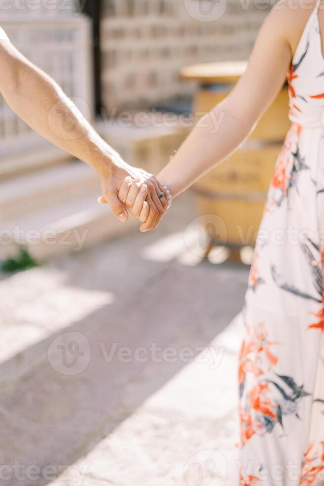 Mens en vrouw zijn staand Aan een zonnig straat Holding handen. bijgesneden. gezichtsloos foto