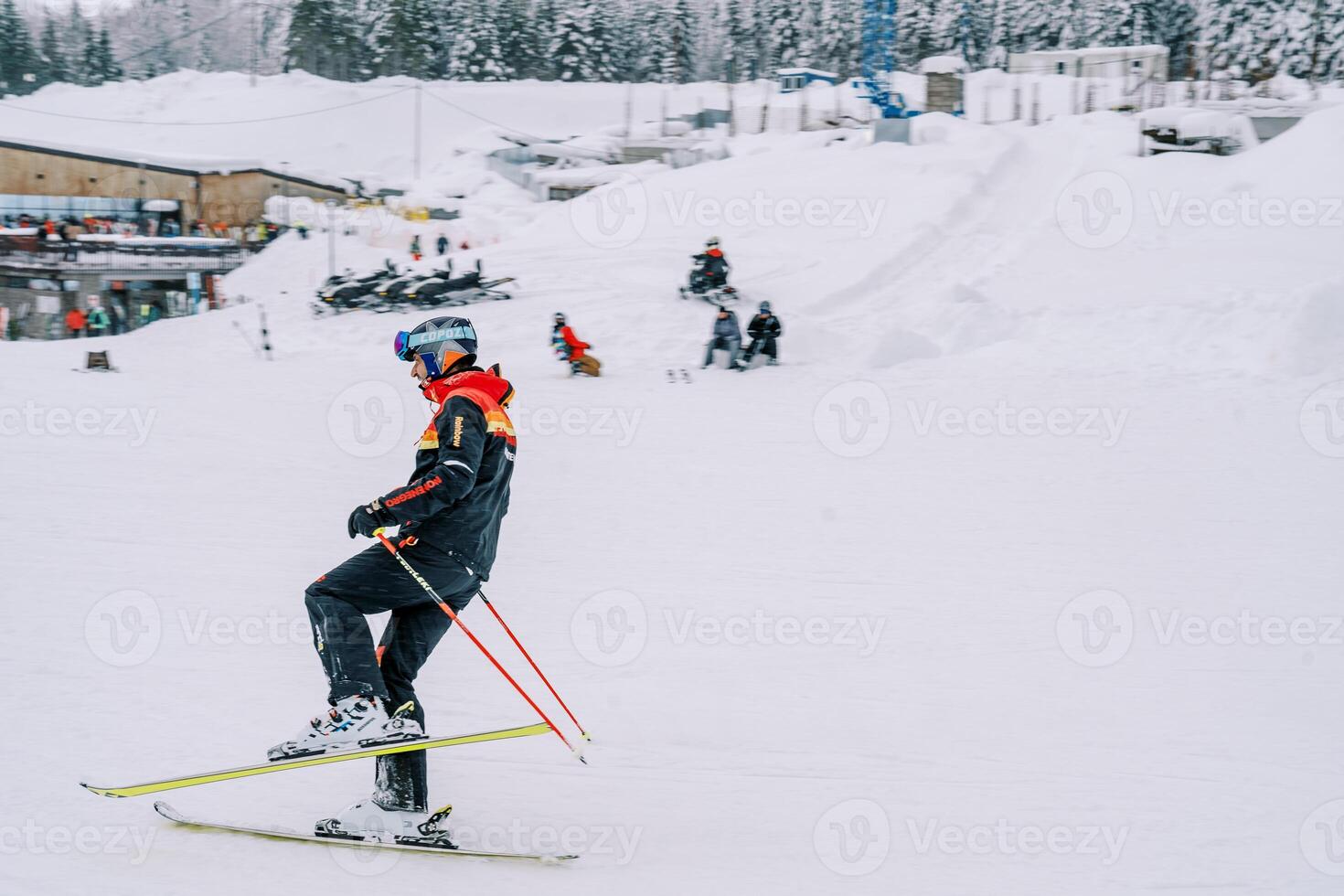 Mens in een ski pak skis met zijn been krom Bij de knie Aan een besneeuwd helling foto